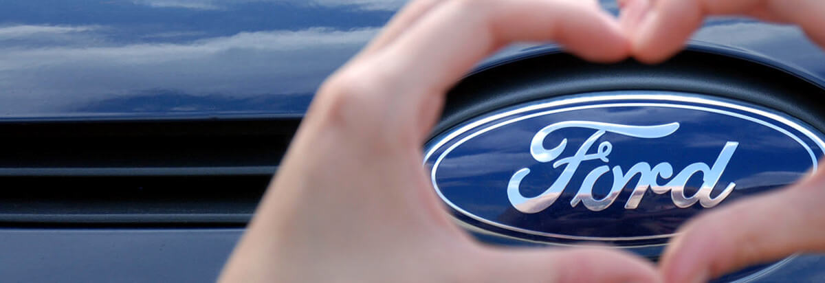 Ein Herz aus zwei Händen um das Ford-Logo auf dem Kühlergrill eines Autos.