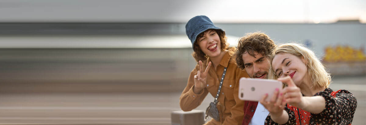 Drei Freunde machen ein Selfie im Freien, lächeln und posieren mit einer Smartphone-Kamera.