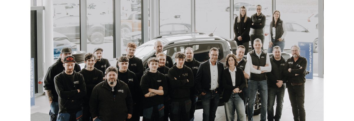 Gruppenfoto eines Autohändler-Teams vor einem Fahrzeug, in einem modernen Showroom.