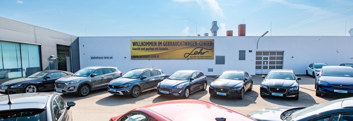 Außenansicht eines Autohauses mit mehreren geparkten Gebrauchtwagen und einem großen Willkommen-Schild.