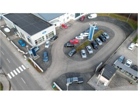 Luftaufnahme eines Autohändlers mit mehreren Autos auf dem Gelände und einem Verkaufsgebäude.