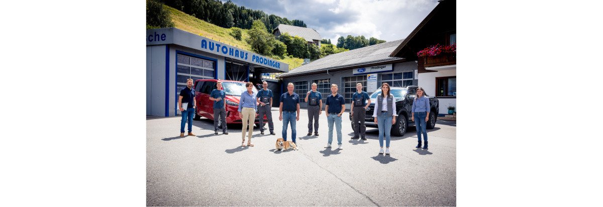 Gruppenfoto vor einem Autohaus mit Technologie- und Service-Mitarbeitern und einem Hund.
