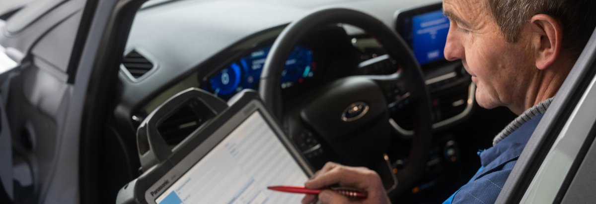 Ein Mann sitzt im Auto und verwendet ein Tablet zur Fahrzeugdiagnose.