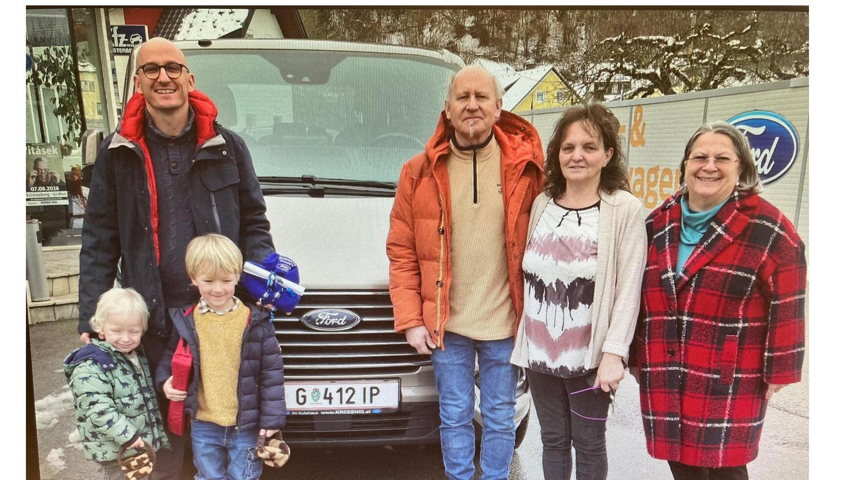 Familienfoto vor einem Ford Fahrzeug, winterliche Kleidung, fünf Personen, zwei Kinder, ländliche Umgebung, neblige Atmosphäre.