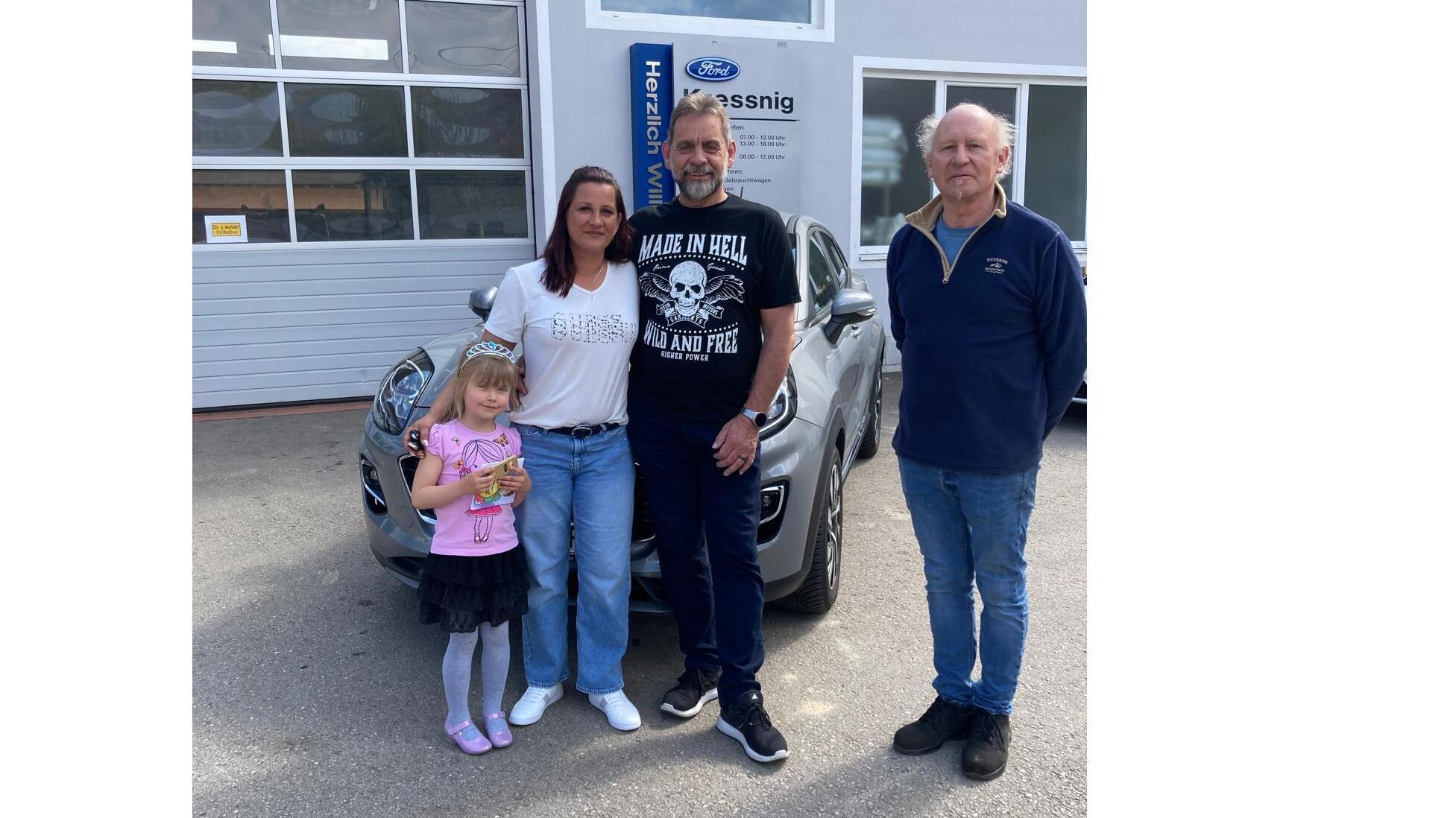 Familie mit kleinem Mädchen und Auto vor einem Ford-Autohaus, sie stehen lächelnd gemeinsam da.