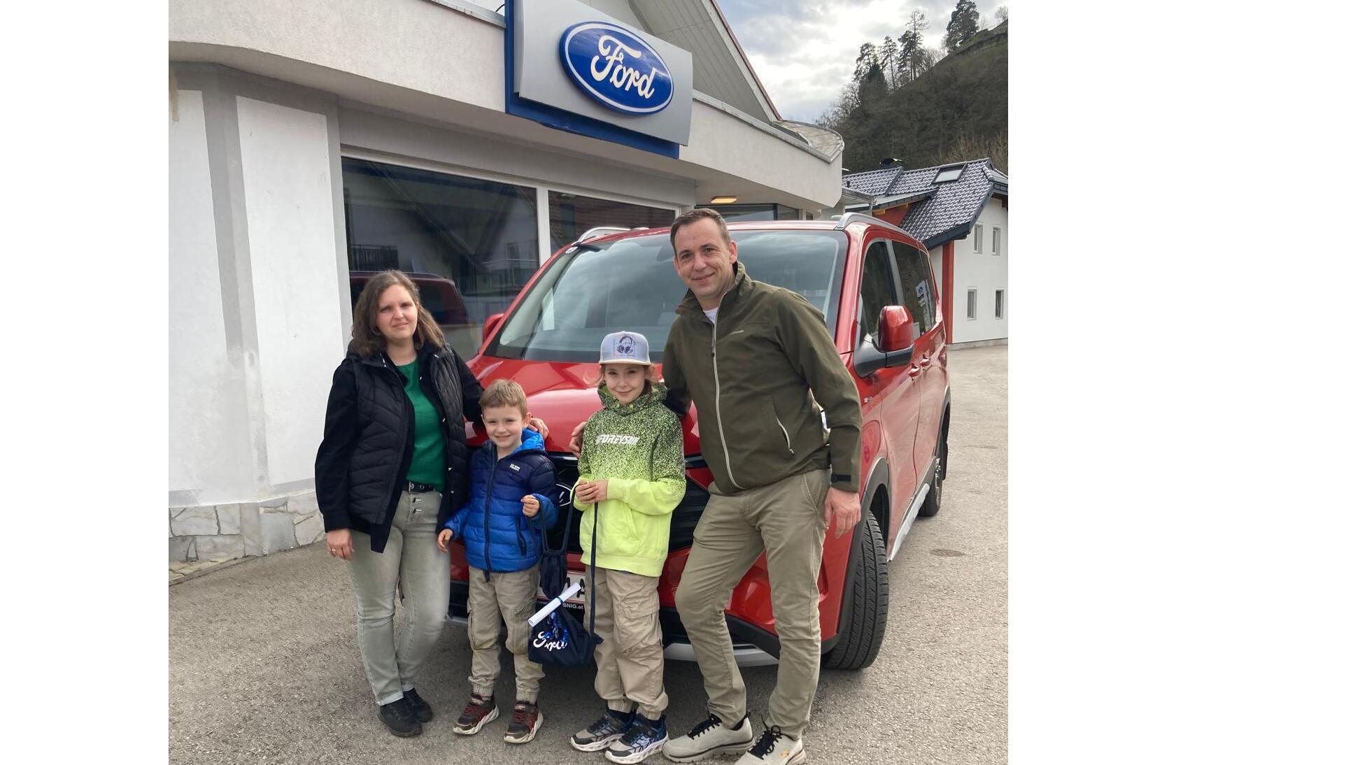Familie steht vor rotem Ford Auto in einem Autohaus, lächelnd mit Autoschlüssel in der Hand.