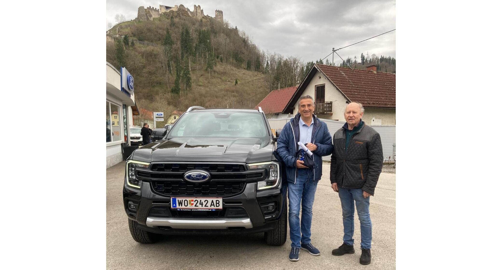 Zwei Männer stehen neben einem schwarzen Ford-Pickup mit einer Burgruine im Hintergrund.