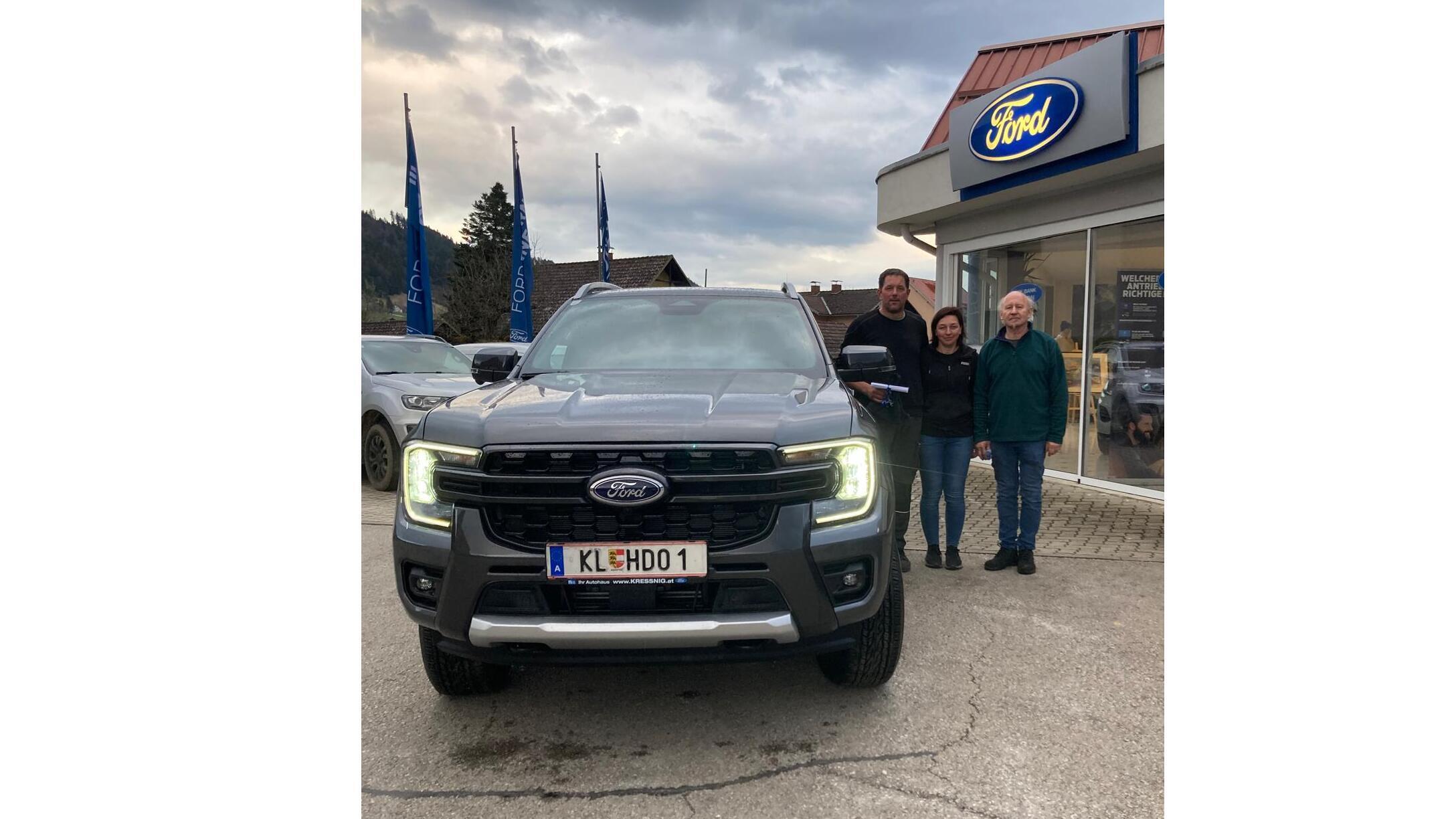 Drei Personen stehen neben einem neuen Ford PKW vor einem Ford Autohaus. Die Atmosphäre ist freundlich und einladend.