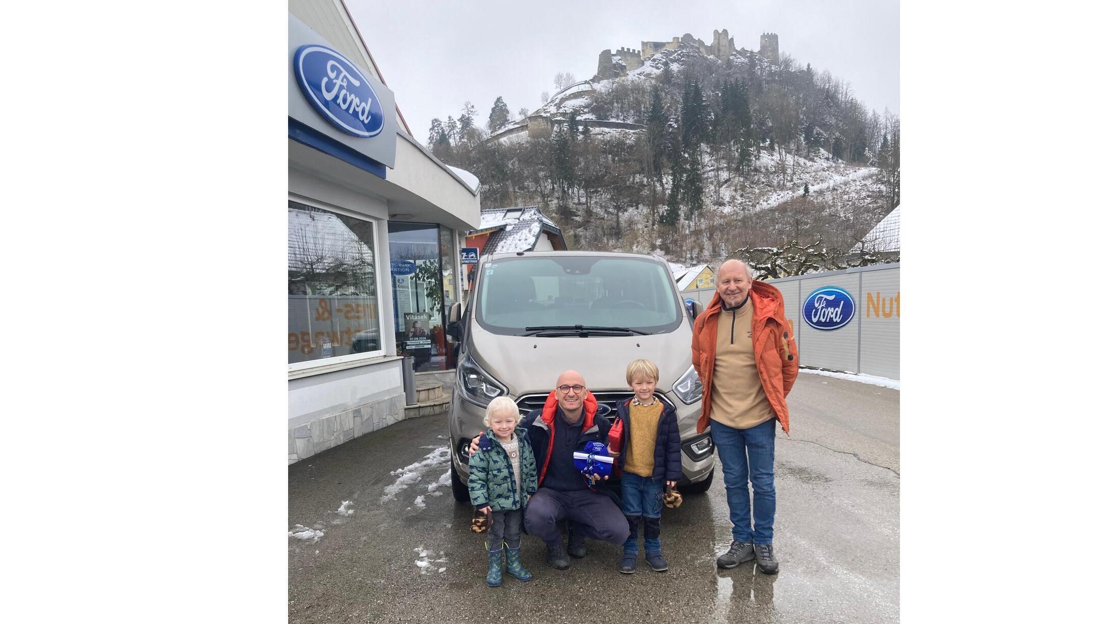 Eine Familie steht vor einem Ford-Auto bei kaltem Wetter, mit einer Burg im Hintergrund.