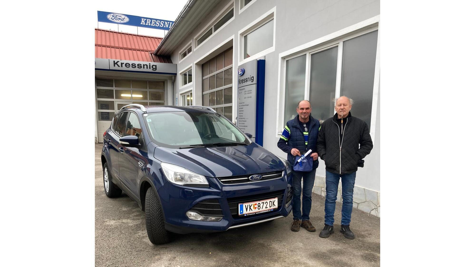Zwei Männer stehen neben einem blauen Ford Kuga vor dem Autohaus Kressnig, eine Fahrzeugübergabe findet statt.