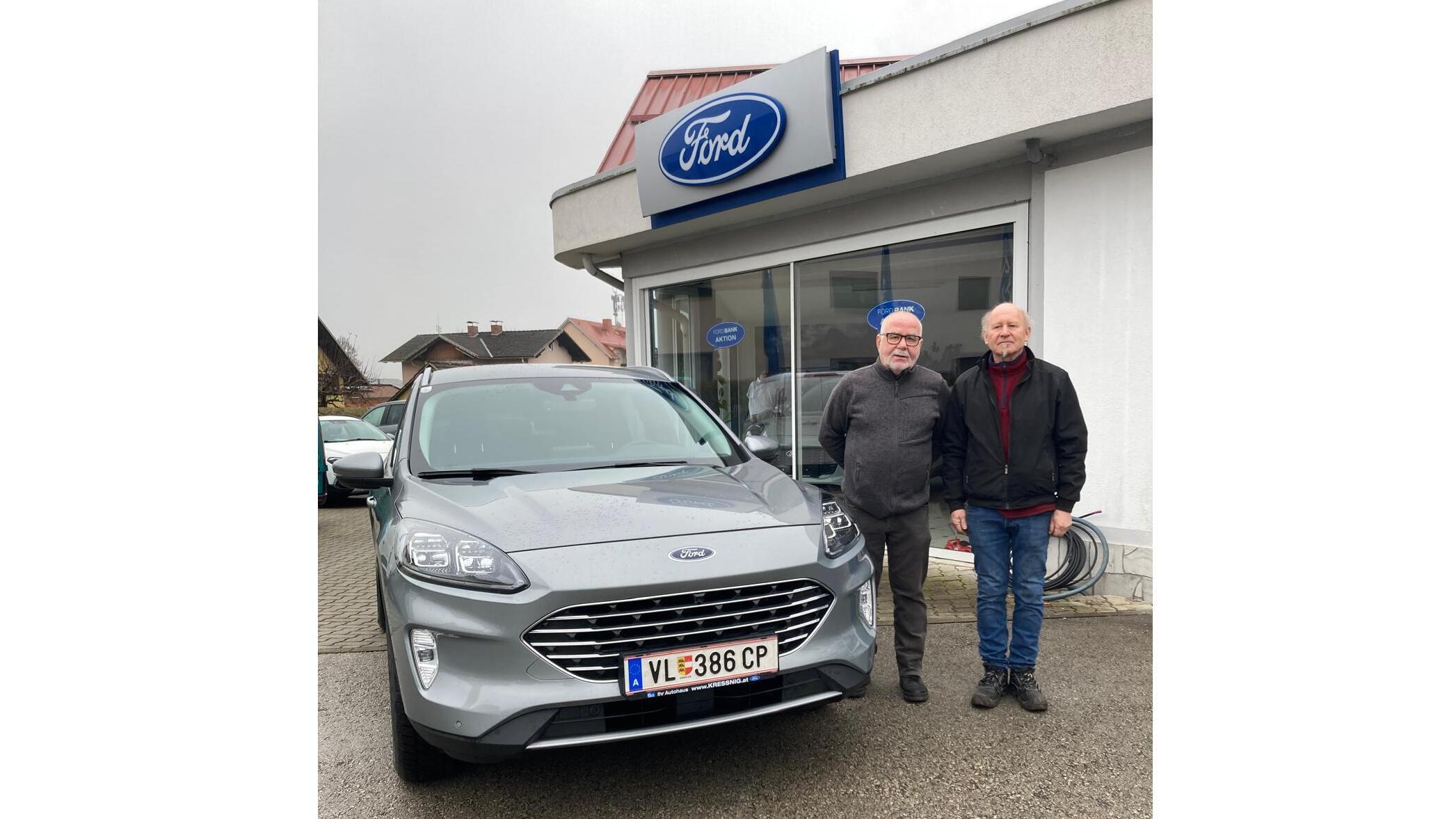 Zwei Männer stehen neben einem grauen Ford SUV vor einem Ford Autohaus.