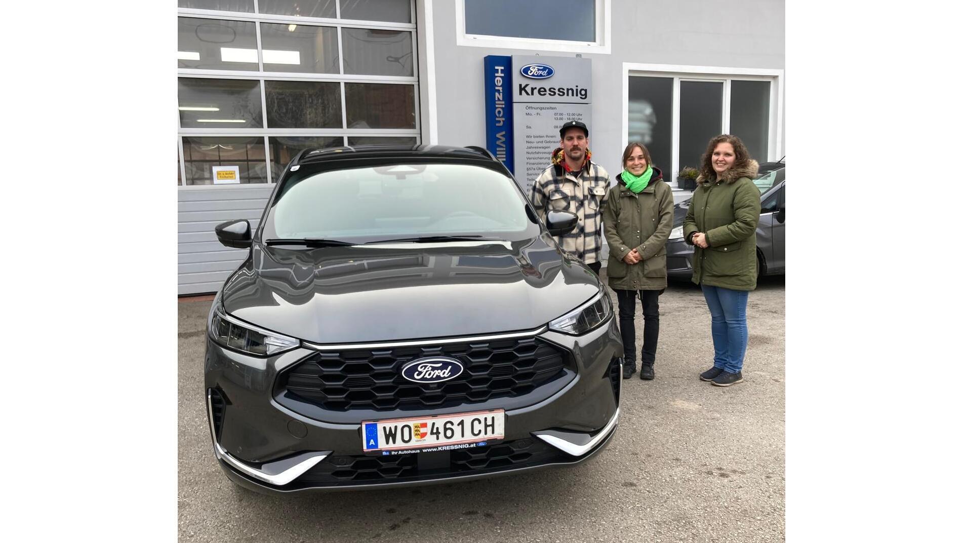 Drei Personen stehen neben einem neuen Ford SUV vor einem Autohaus. Freundliche Atmosphäre und glänzendes Fahrzeug.