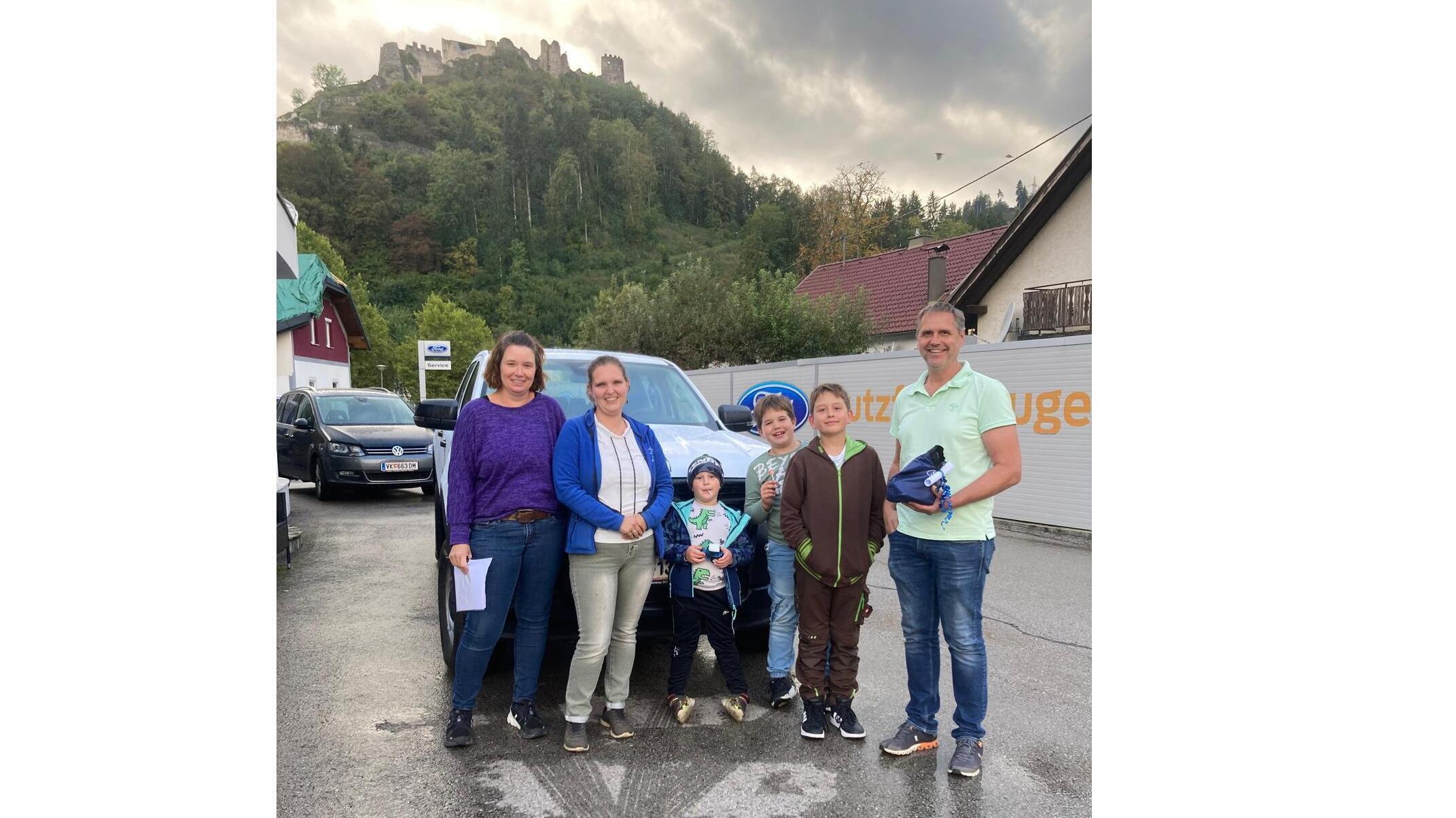Gruppe von Erwachsenen und Kindern vor einem Auto mit einer Burg im Hintergrund, aufgenommen an einem herbstlichen Tag.