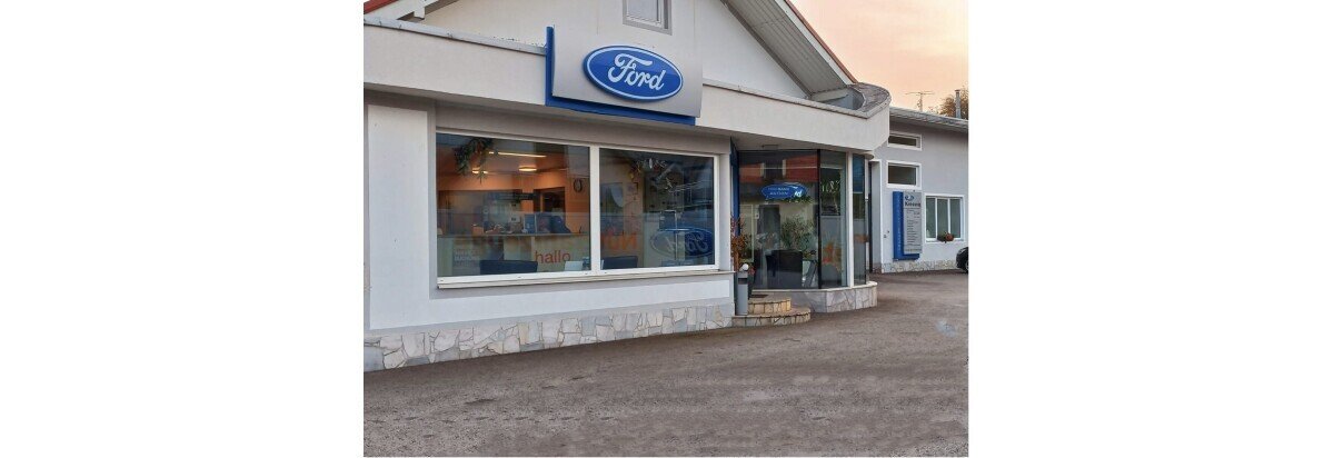 Ford Autohaus mit großem Schaufenster, geparktem Fahrzeug und einladendem Eingangsbereich.