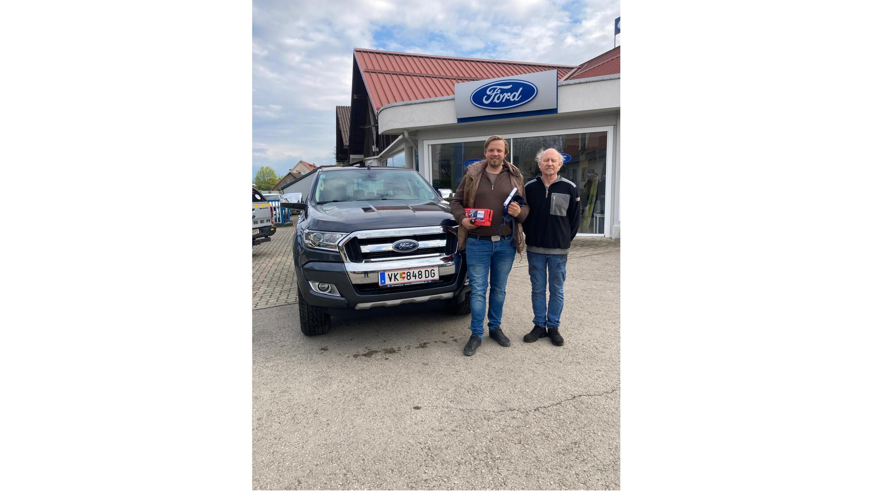 Zwei Männer stehen neben einem schwarzen Ford in einem Autohaus mit Ford-Schild.