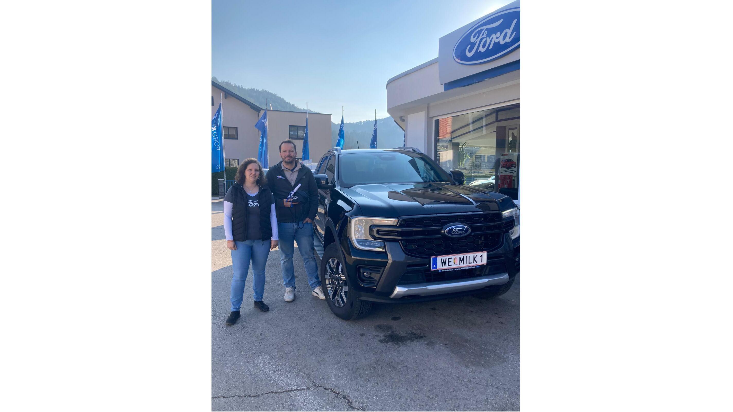 Ein Mann und eine Frau stehen neben einem neuen schwarzen Ford in einem Autohaus.