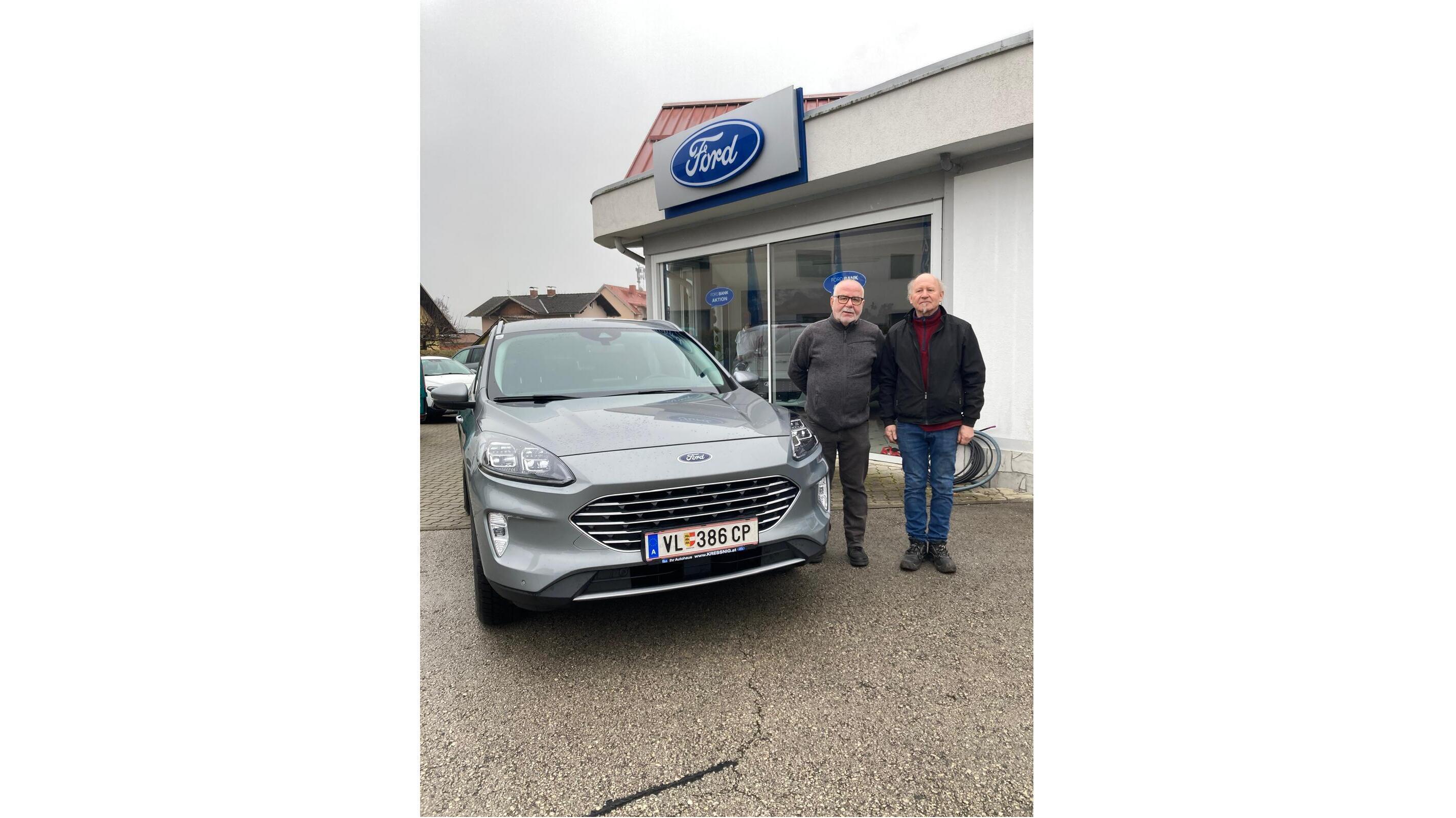 Zwei Männer stehen neben einem grauen Ford SUV vor einem Ford Autohaus.