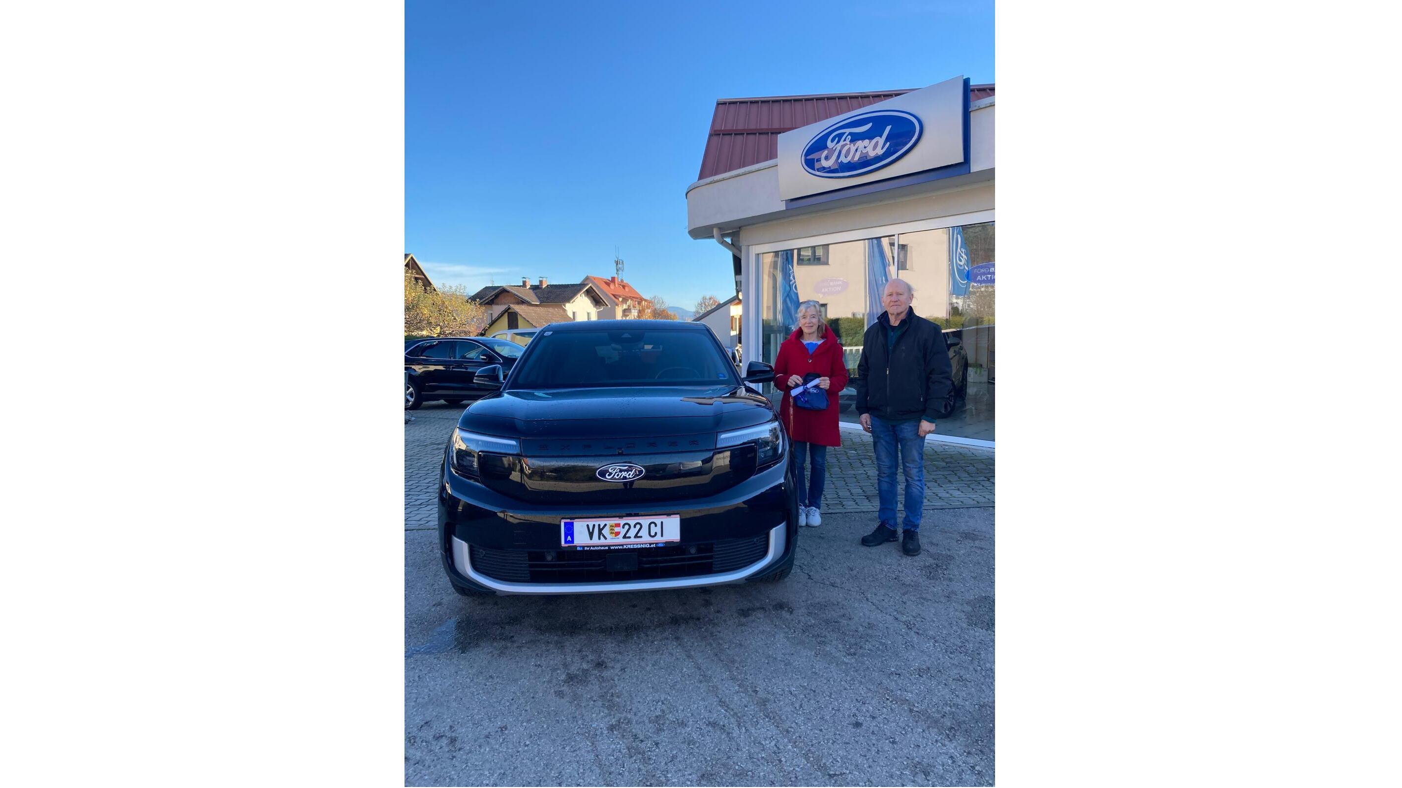 Ein Paar steht vor einem schwarzen Ford-Auto vor einem Autohaus mit Ford-Schild.