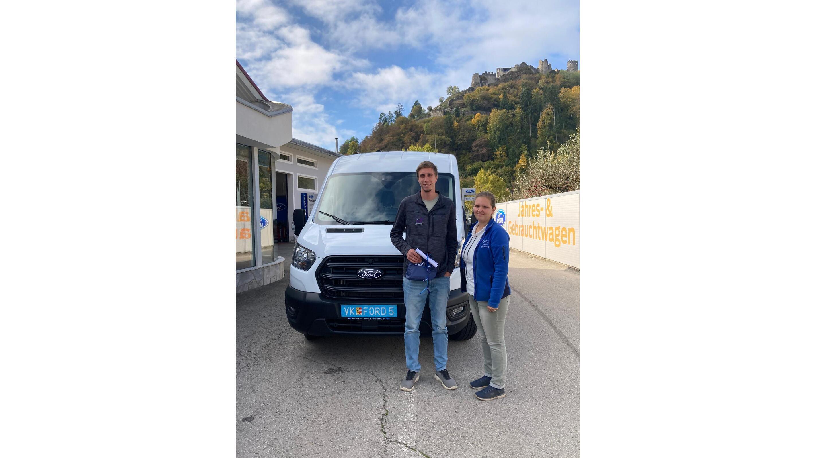 Zwei Personen gemeinsam vor einem weißen Ford Transporter, mit einer Landschaft im Hintergrund.