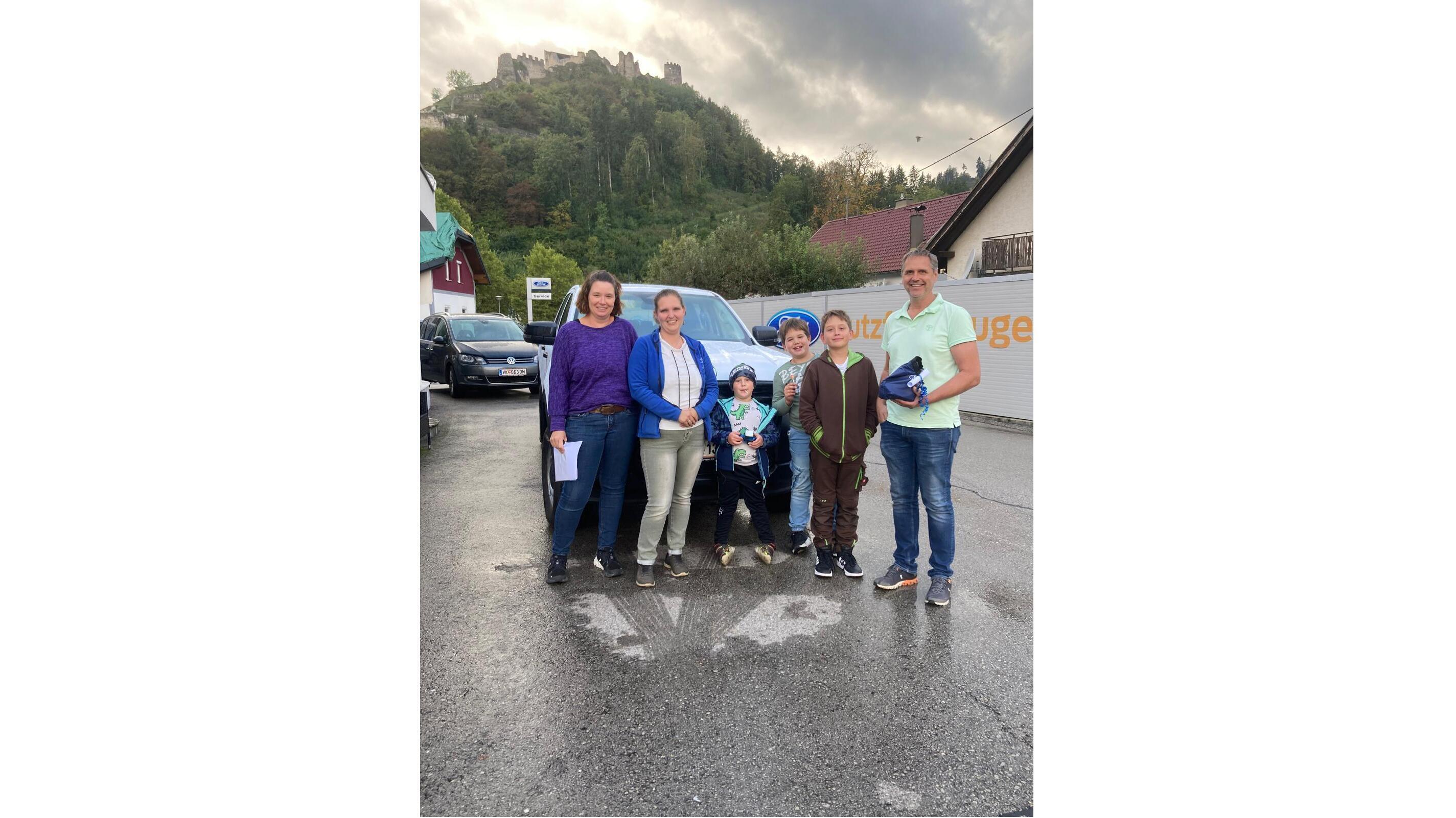 Gruppe von fünf Personen steht auf einer Straße, mit einer Burgruine im Hintergrund und grauem Himmel.