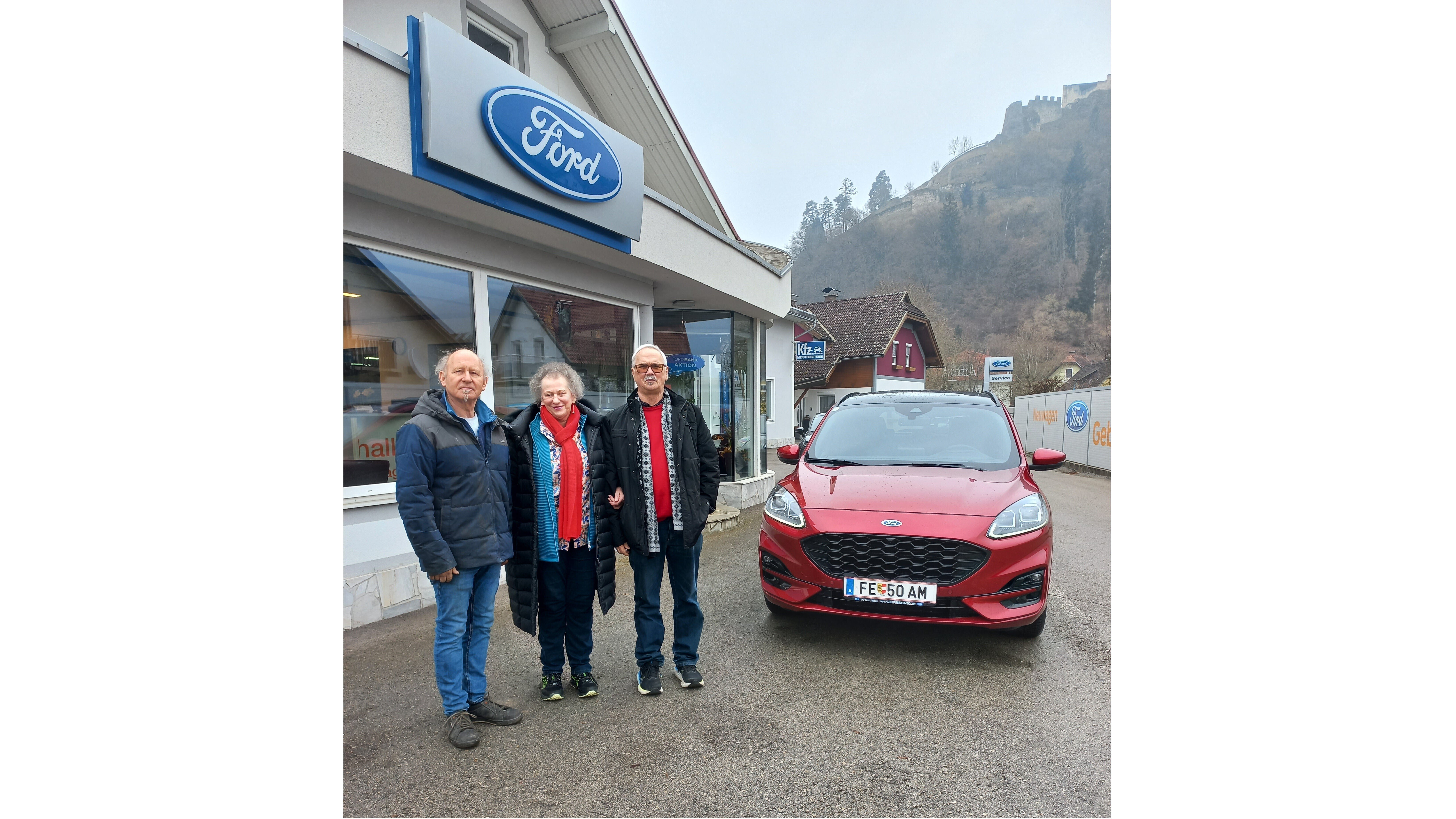 Eine Gruppe steht vor einem Ford-Händler mit einem roten Ford-Auto im Vordergrund.