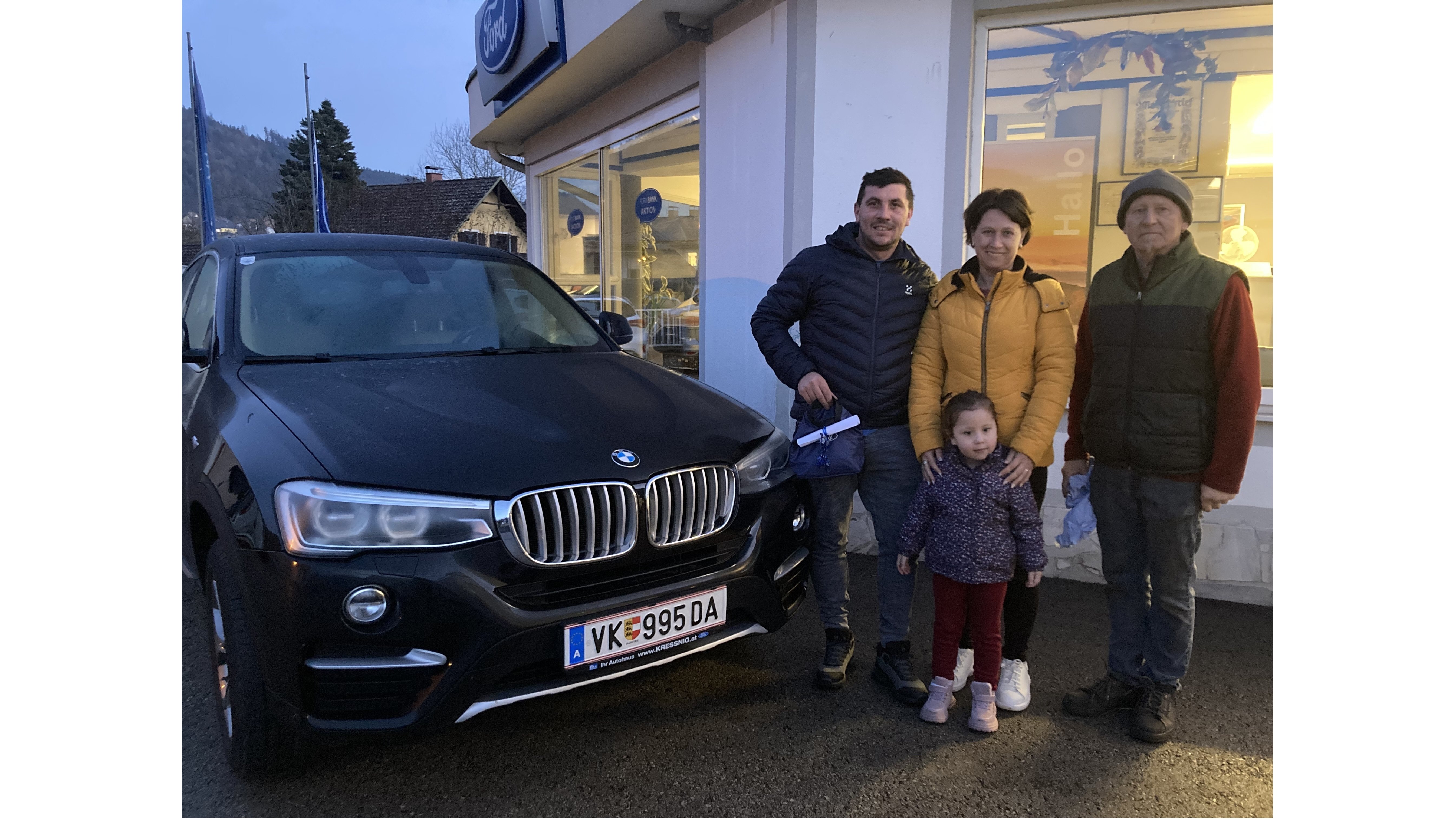 Familie steht neben einem schwarzen BMW, in einer kühlen Abendatmosphäre, beim Autokauf.