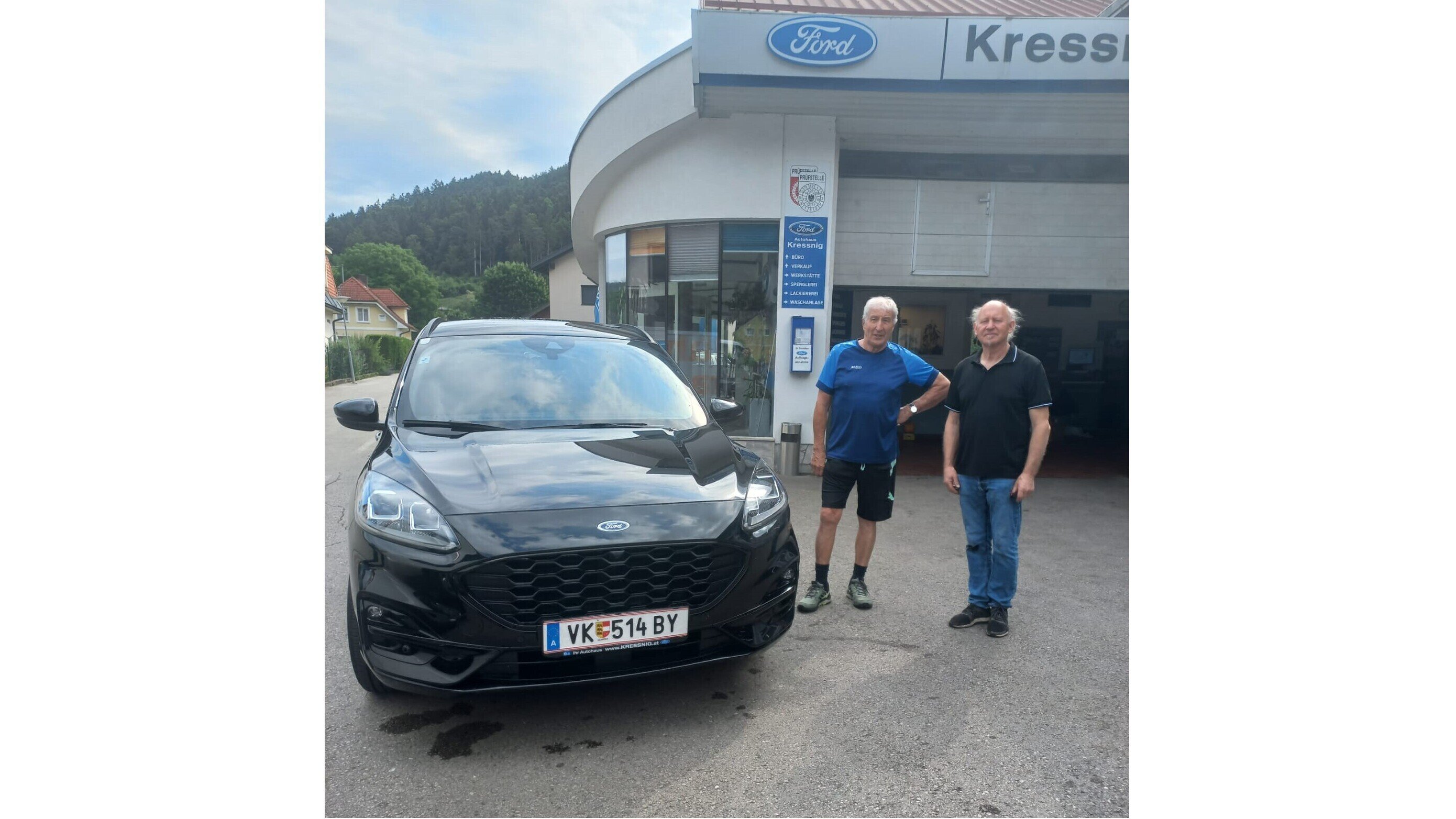Zwei Männer stehen neben einem schwarzen Ford Auto vor einem Ford-Servicezentrum.