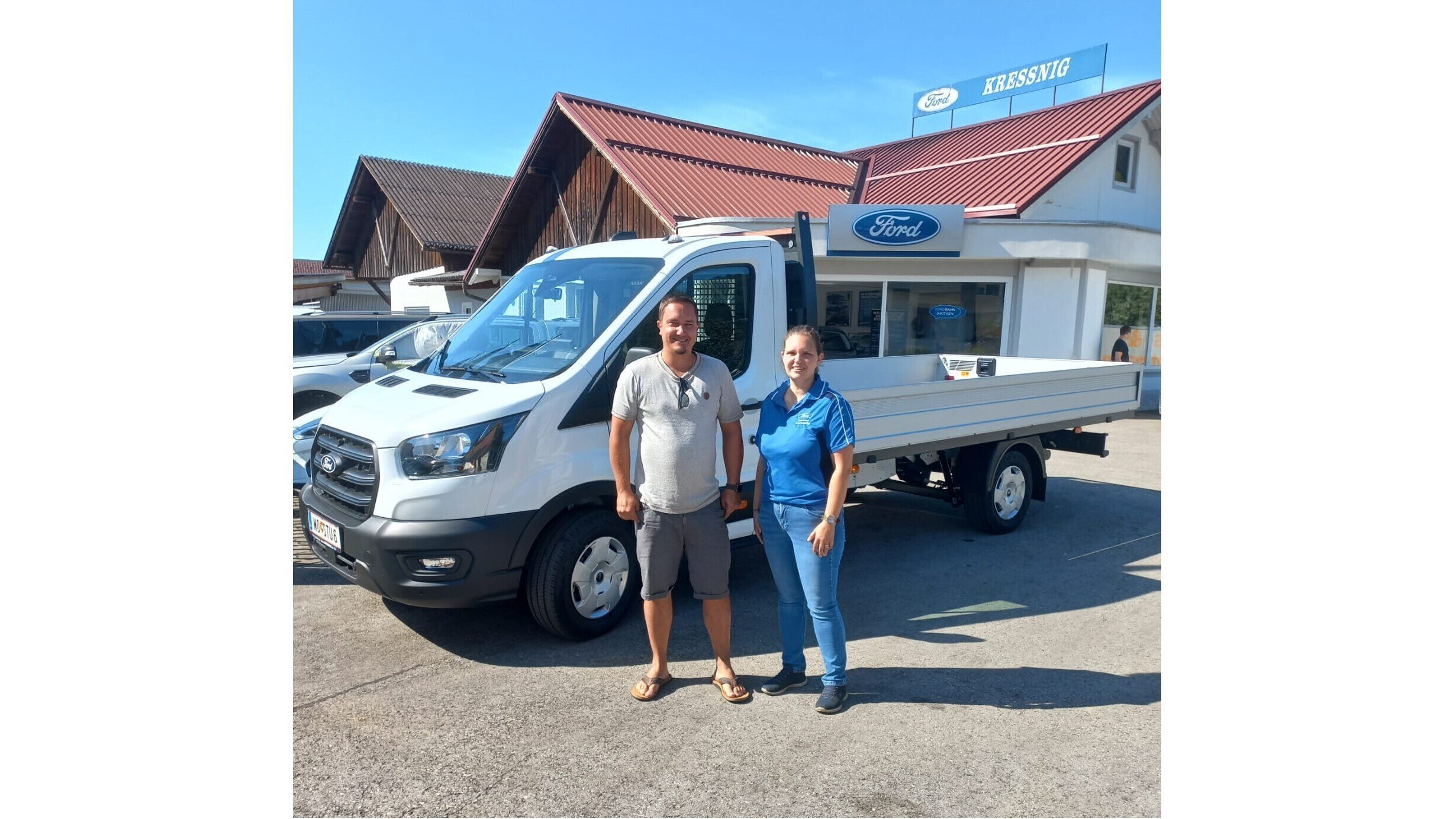 Ein Mann und eine Frau stehen neben einem Ford Transit Nutzfahrzeug vor einem Autohaus.