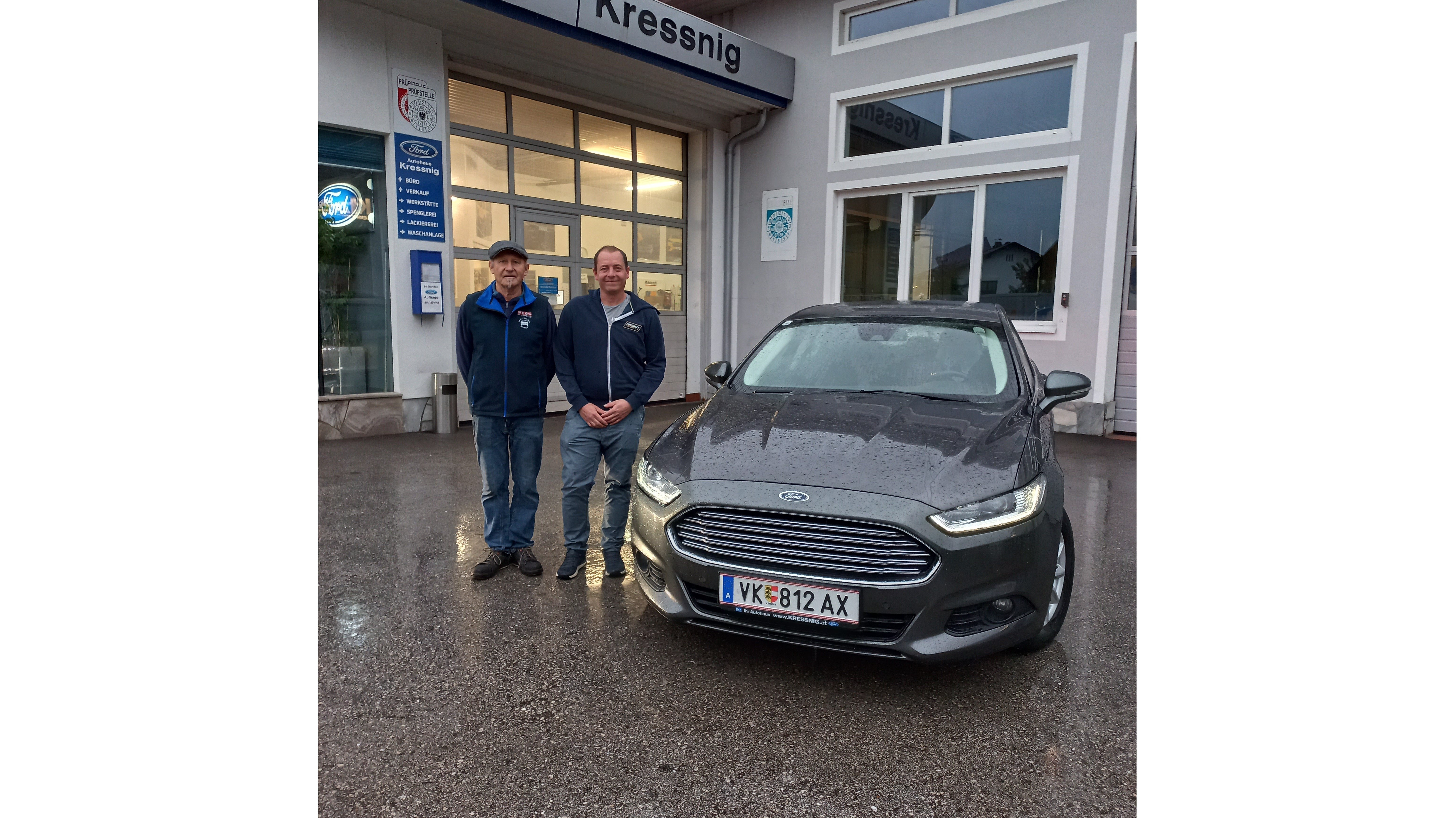 Zwei Männer stehen neben einem grauen Ford vor dem Autohaus Kressnig, es regnet leicht.