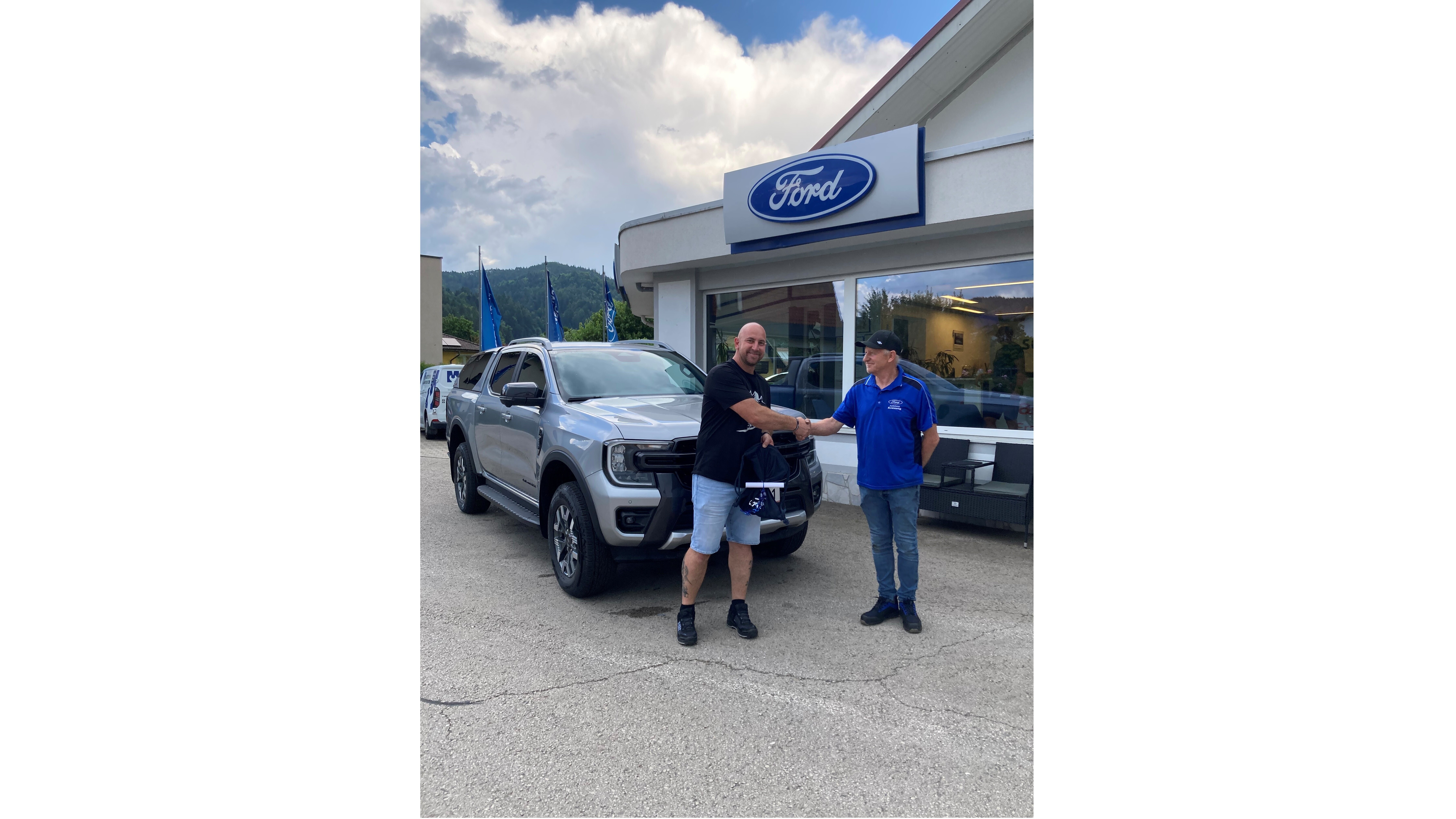 Zwei Männer schütteln die Hände vor einem grauen Ford Fahrzeug in einem Autohaus.