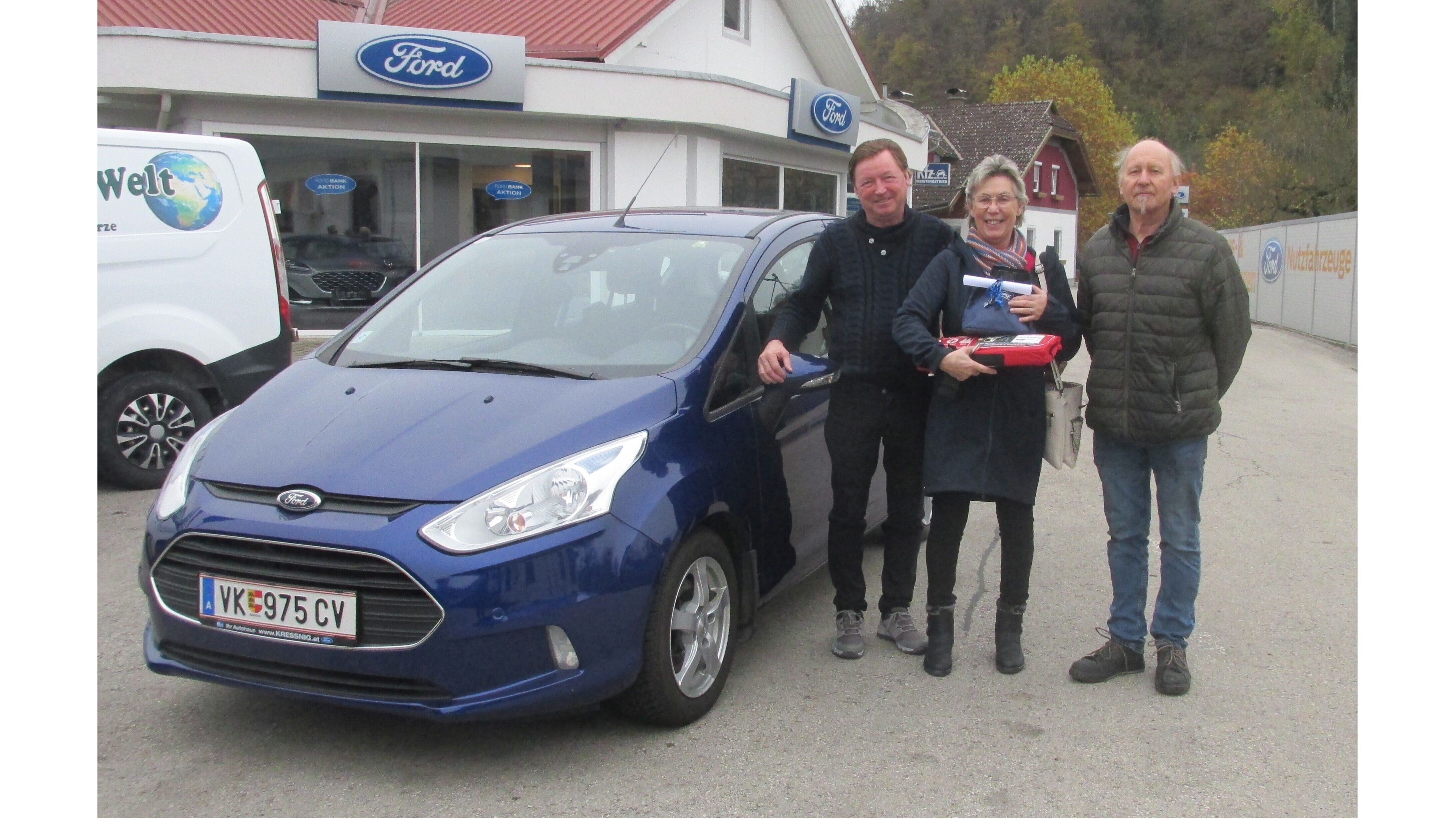 Drei Personen stehen neben einem blauen Ford in einem Autohaus. Hintergrund mit Ford-Schild sichtbar.