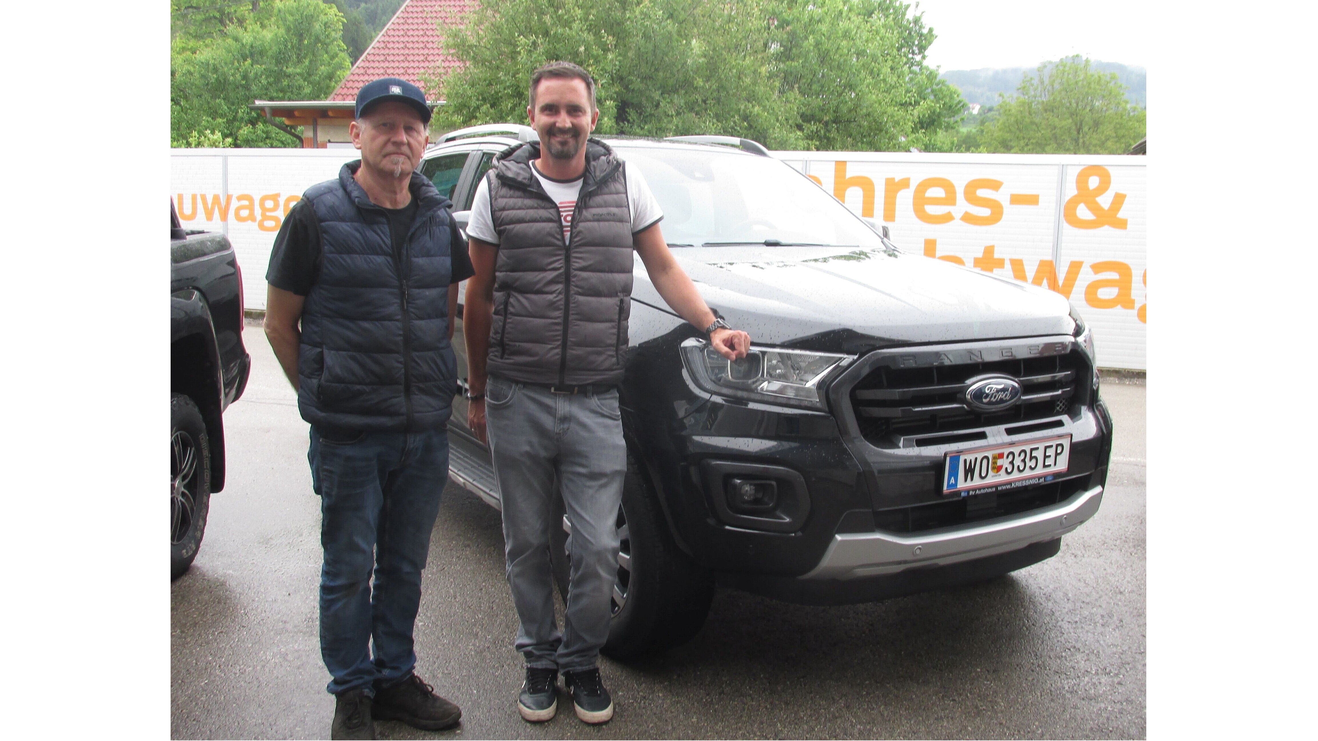 Zwei Männer stehen neben einem schwarzen Ford-Pickup, umgeben von grüner Natur und einem Zaun.