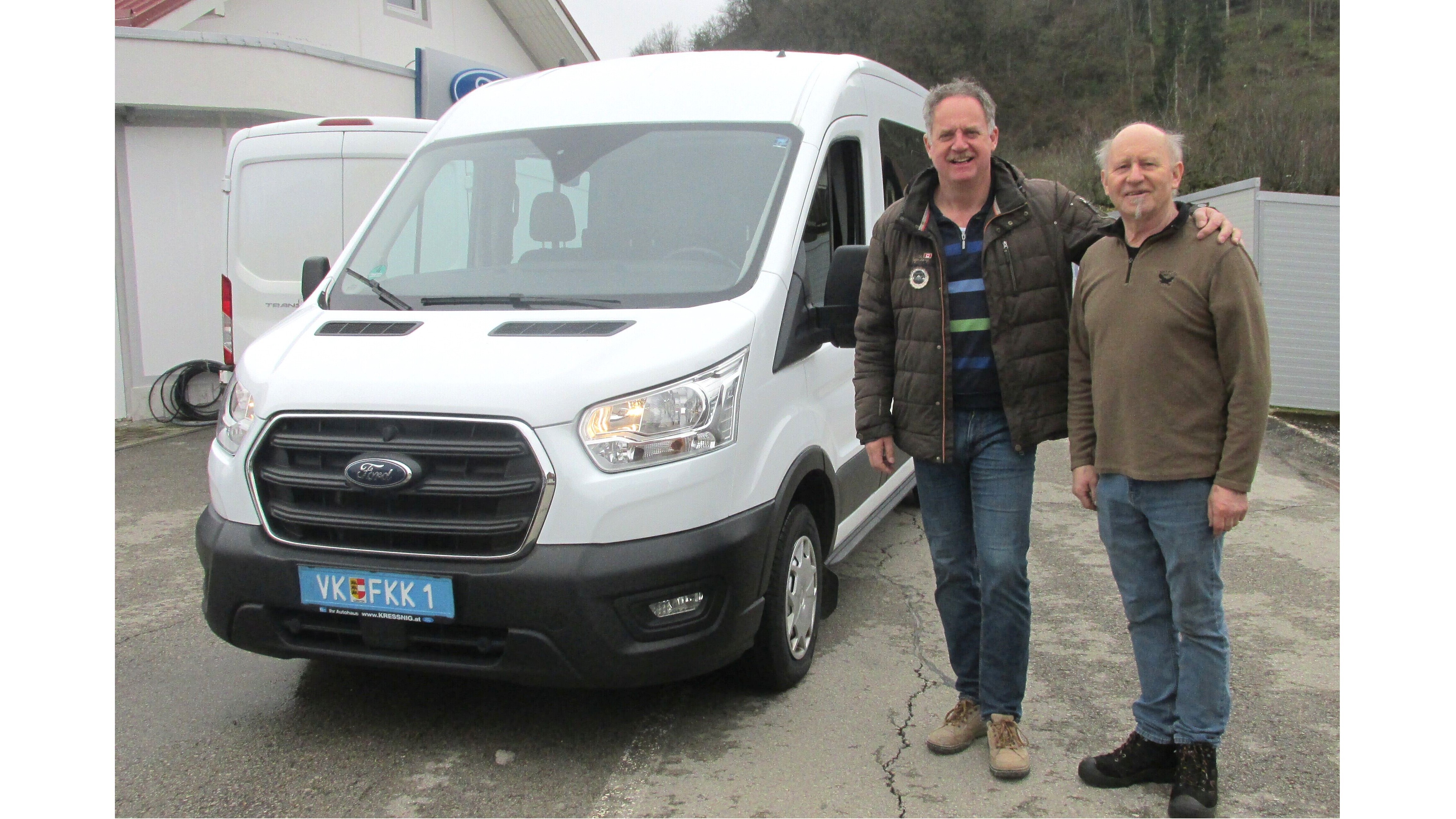 Zwei Männer stehen neben einem weißen Ford Transit, lächeln in die Kamera, vor einem Gebäude.