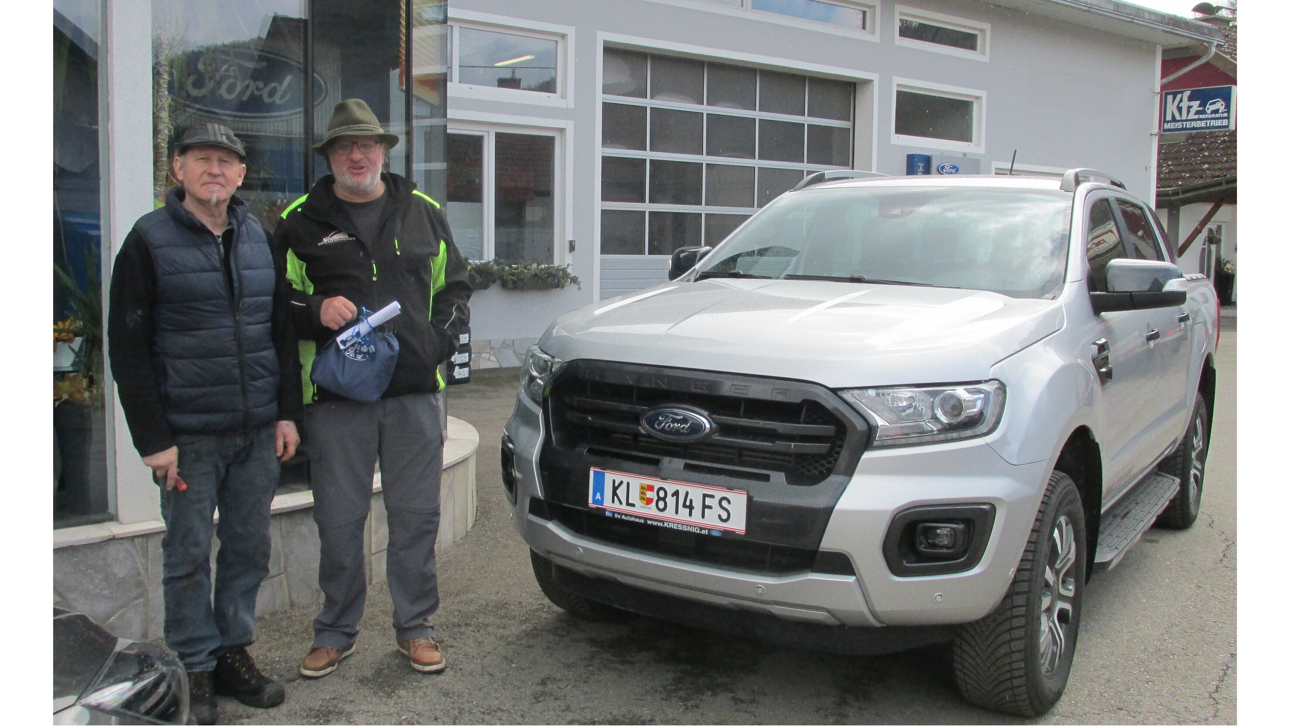 Zwei Männer stehen neben einem silbernen Ford Ranger vor einer Werkstatt. Das Geschäft hat große Fenster und eine moderne Fassade.