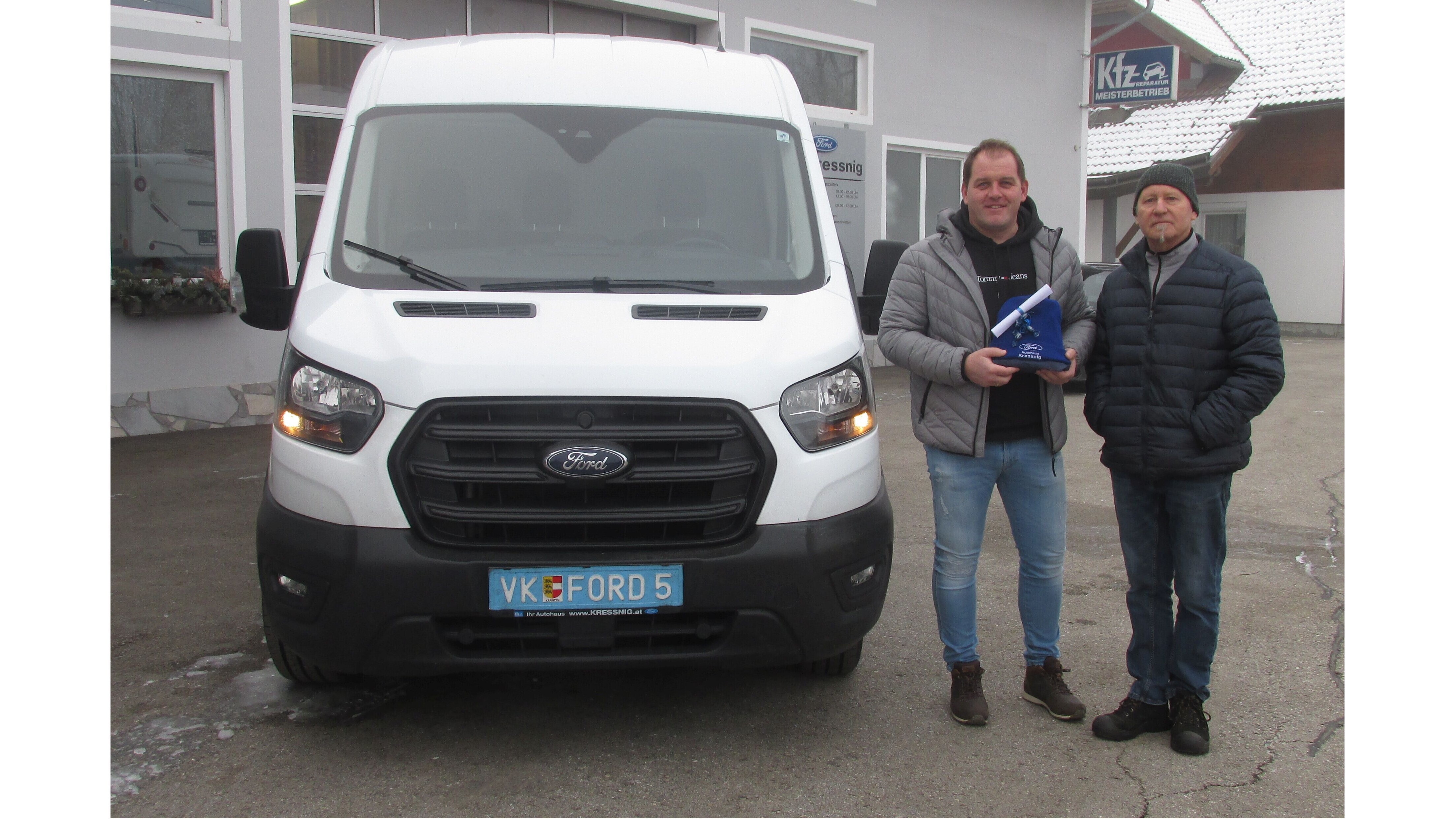 Ein neues Fahrzeug: Ein Mann hält einen Preis neben einem Ford Transit vor einem Kfz-Betrieb im Winter.