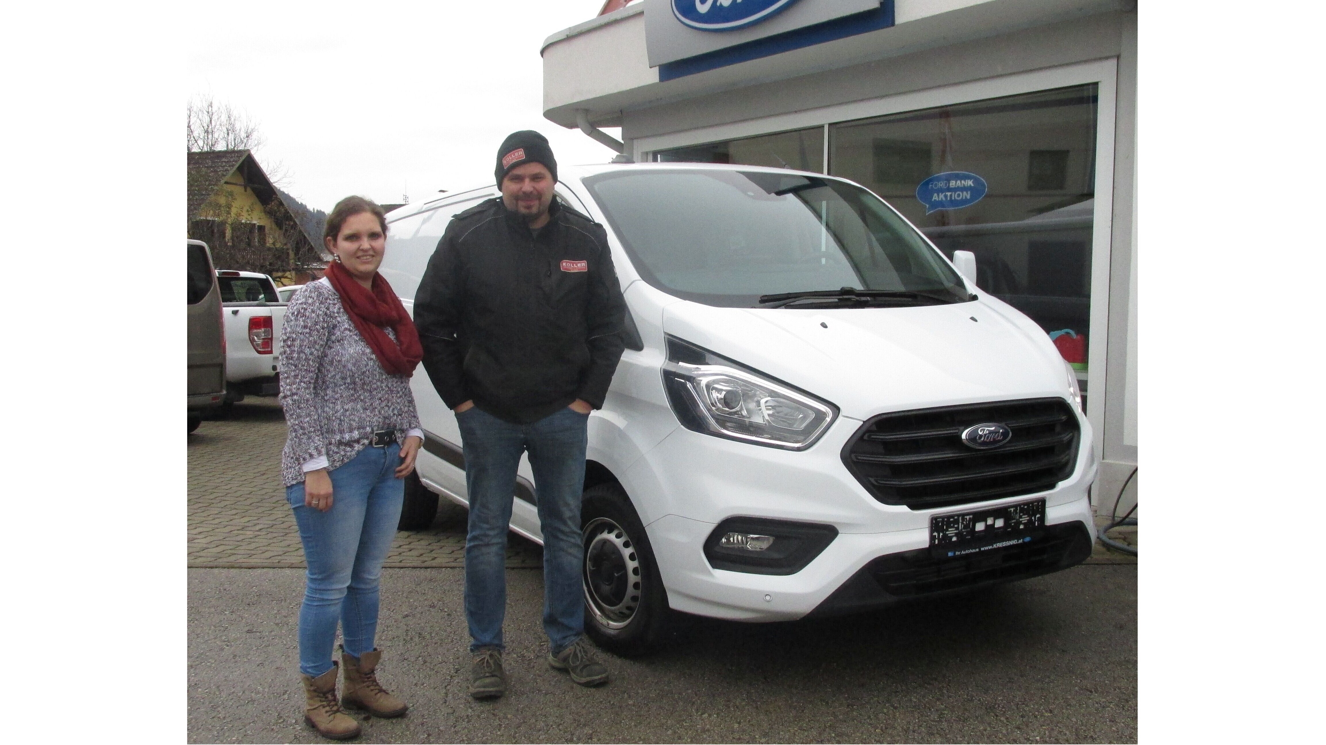 Zwei Personen stehen neben einem weißen Ford Transporter vor einem Autohaus.