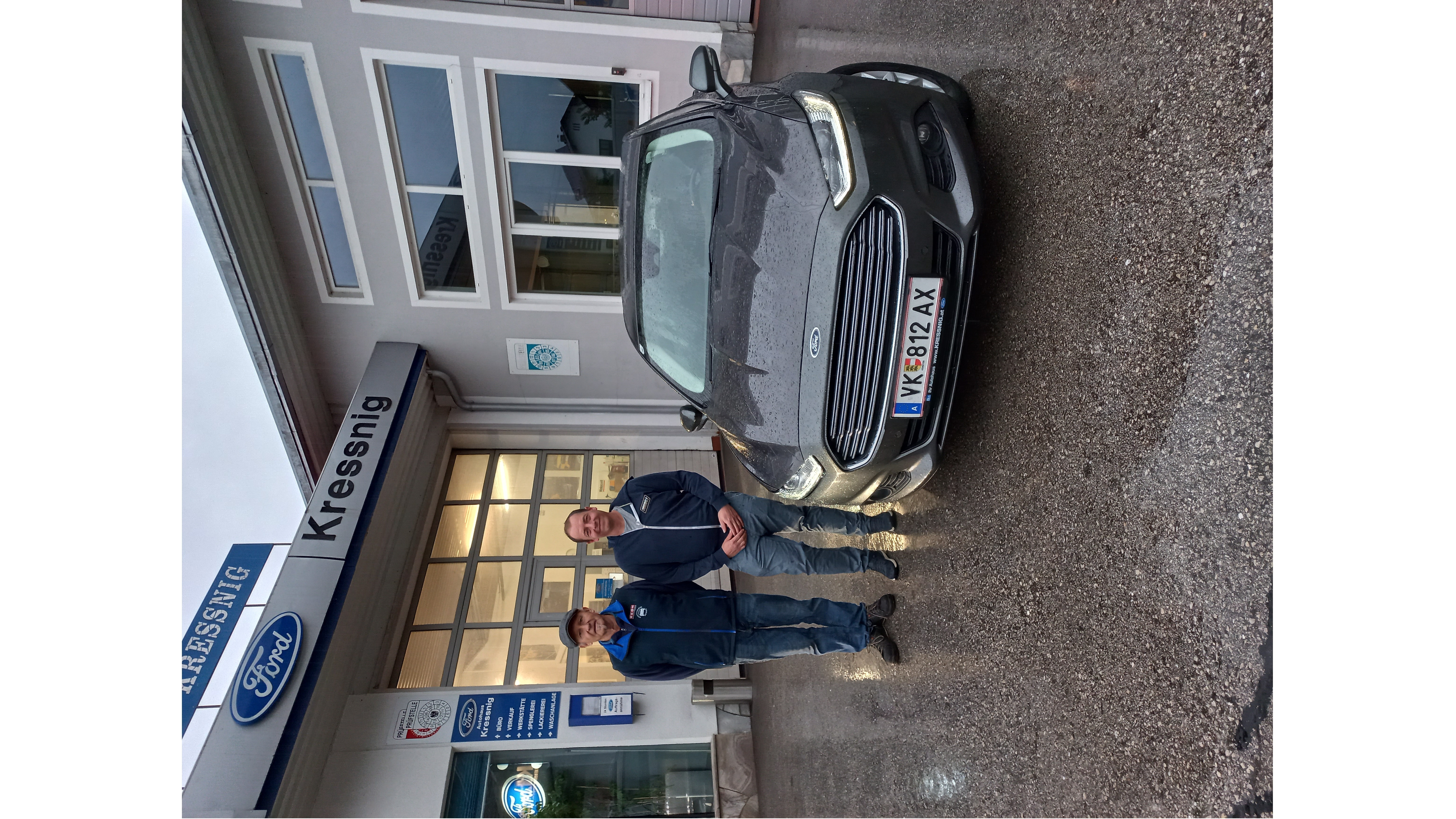 Zwei Männer stehen neben einem Ford-Auto vor einem Autohändler mit dem Namen Kressnig.