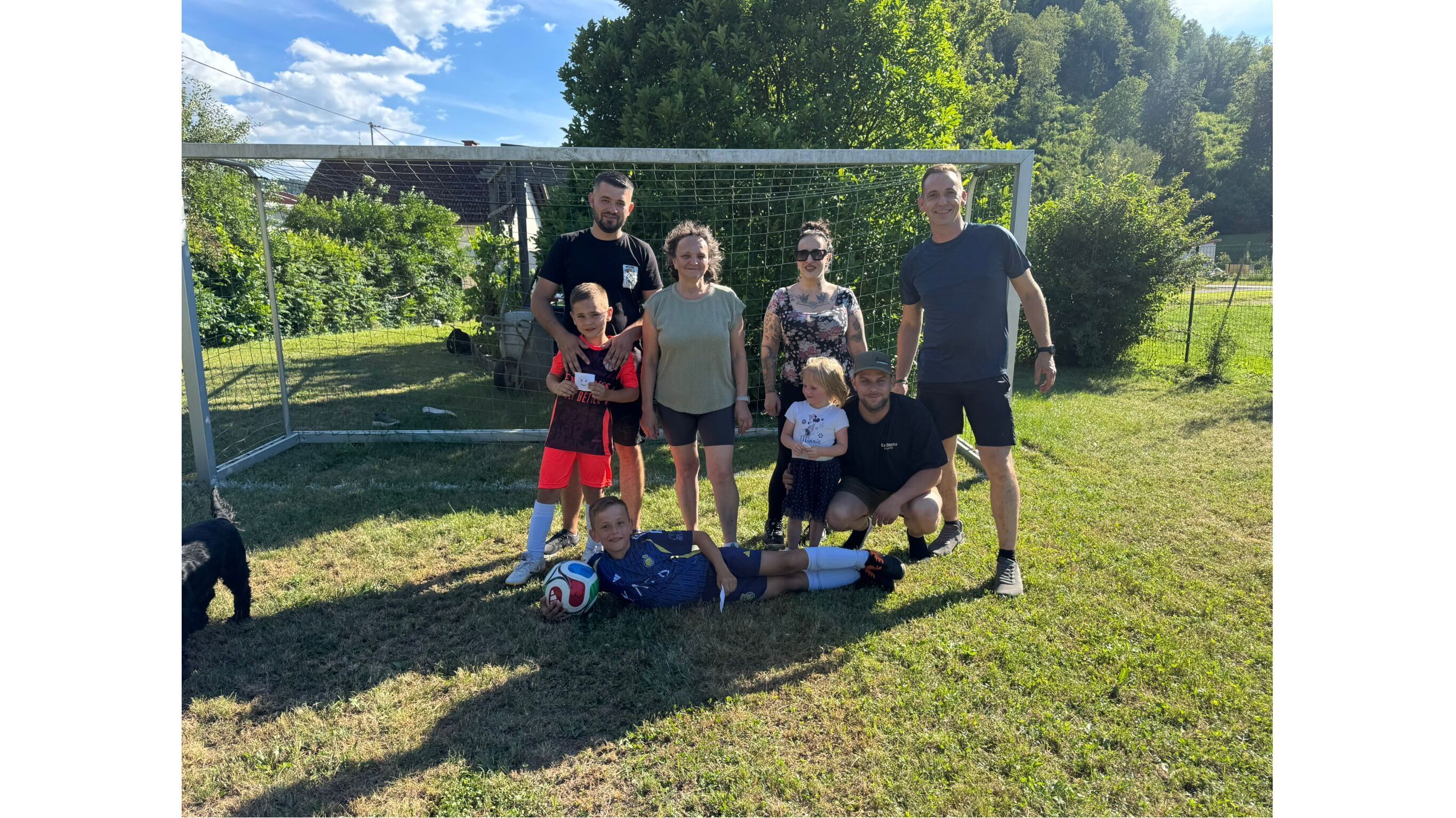 Eine Gruppe von Erwachsenen und Kindern posiert auf einem Fußballfeld, umgeben von Natur.