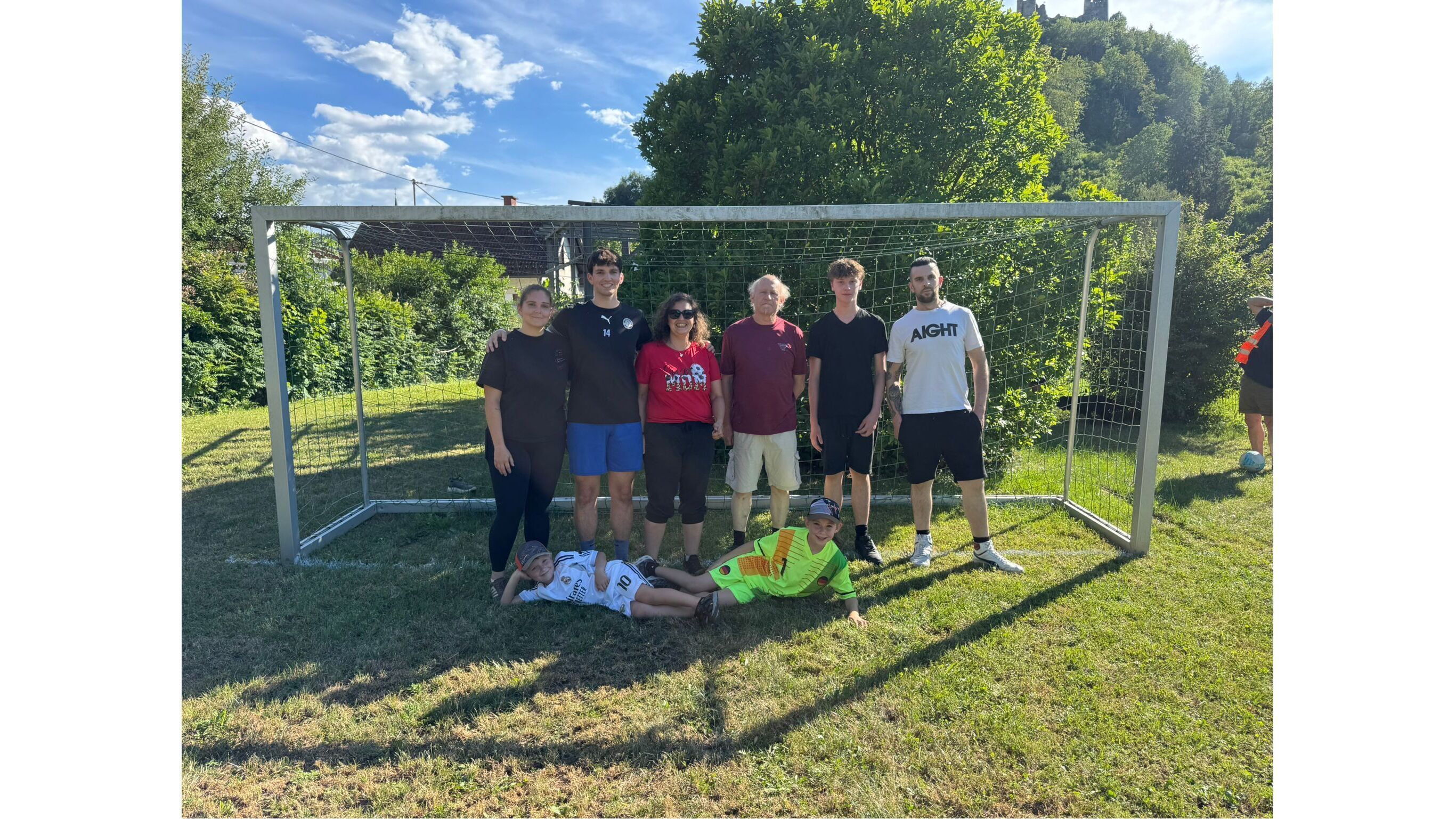 Gruppe von Menschen vor einem Fußballtor im Freien, alle lächeln und posieren für ein Foto.