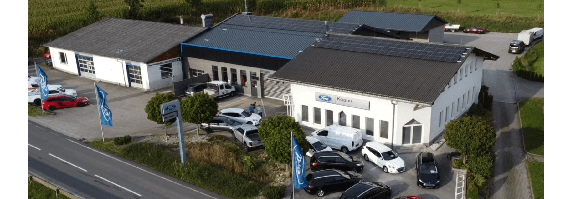 Luftaufnahme eines Ford-Autohauses mit mehreren Fahrzeugen und Solarpanelen auf dem Dach.
