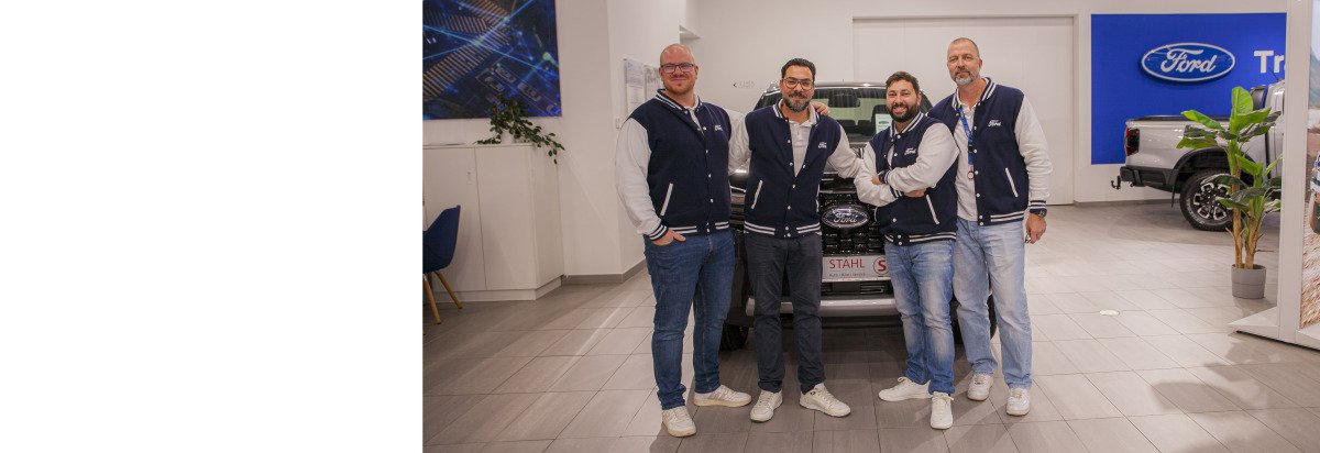 Vier Männer in Sportjacken stehen vor einem Ford-Auto in einem modernen Showroom.