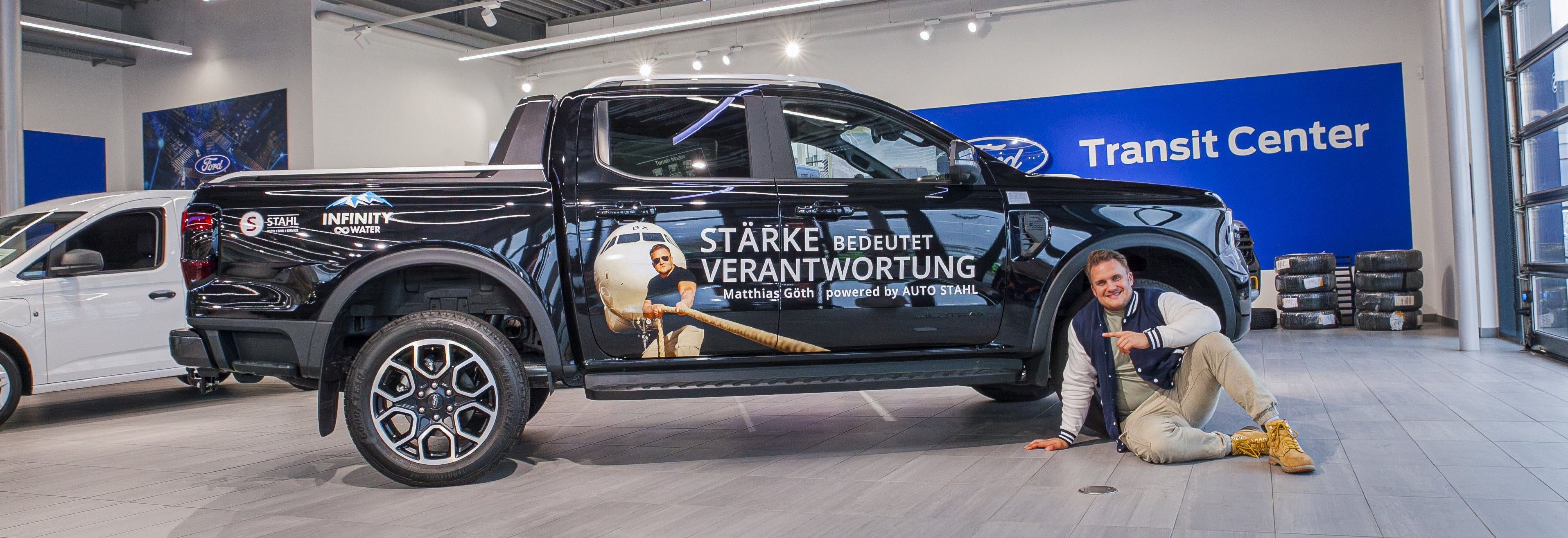 Ein schwarzer Pickup-Truck im Ford Transit Center, mit Werbung für Stärke und Verantwortung, neben einer Person, die posiert.