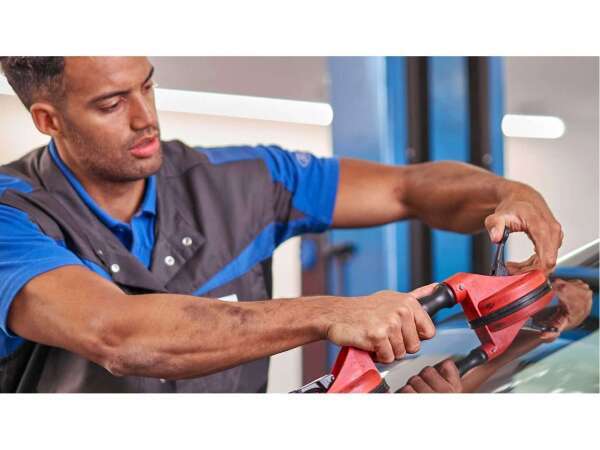 Ein Mechaniker repariert eine Autoscheibe mit einem speziellen Werkzeug in einer Werkstatt.