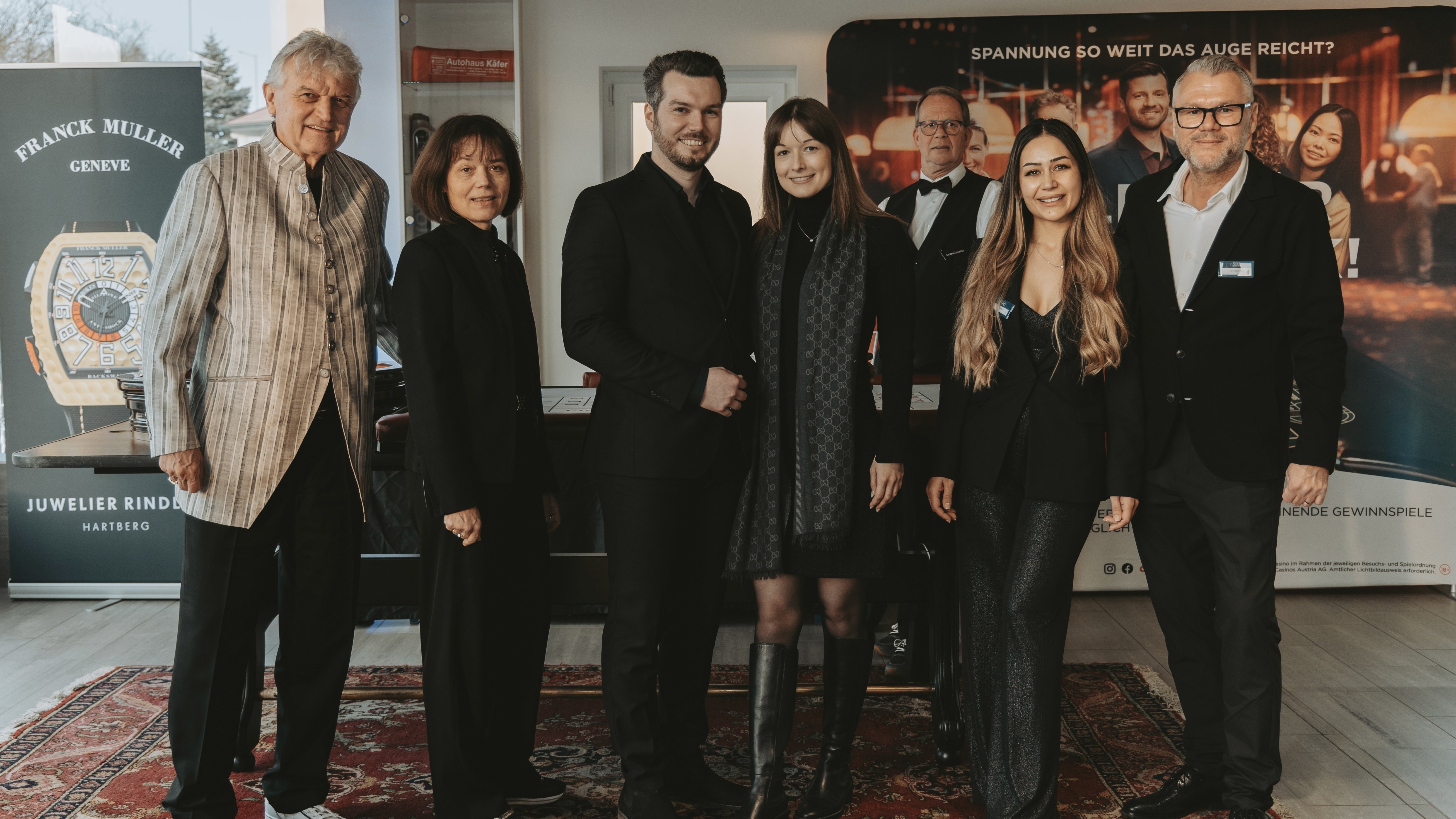 Gruppe von Menschen in eleganter Kleidung, posierend vor einem Franck Müller Banner bei einer Veranstaltung.