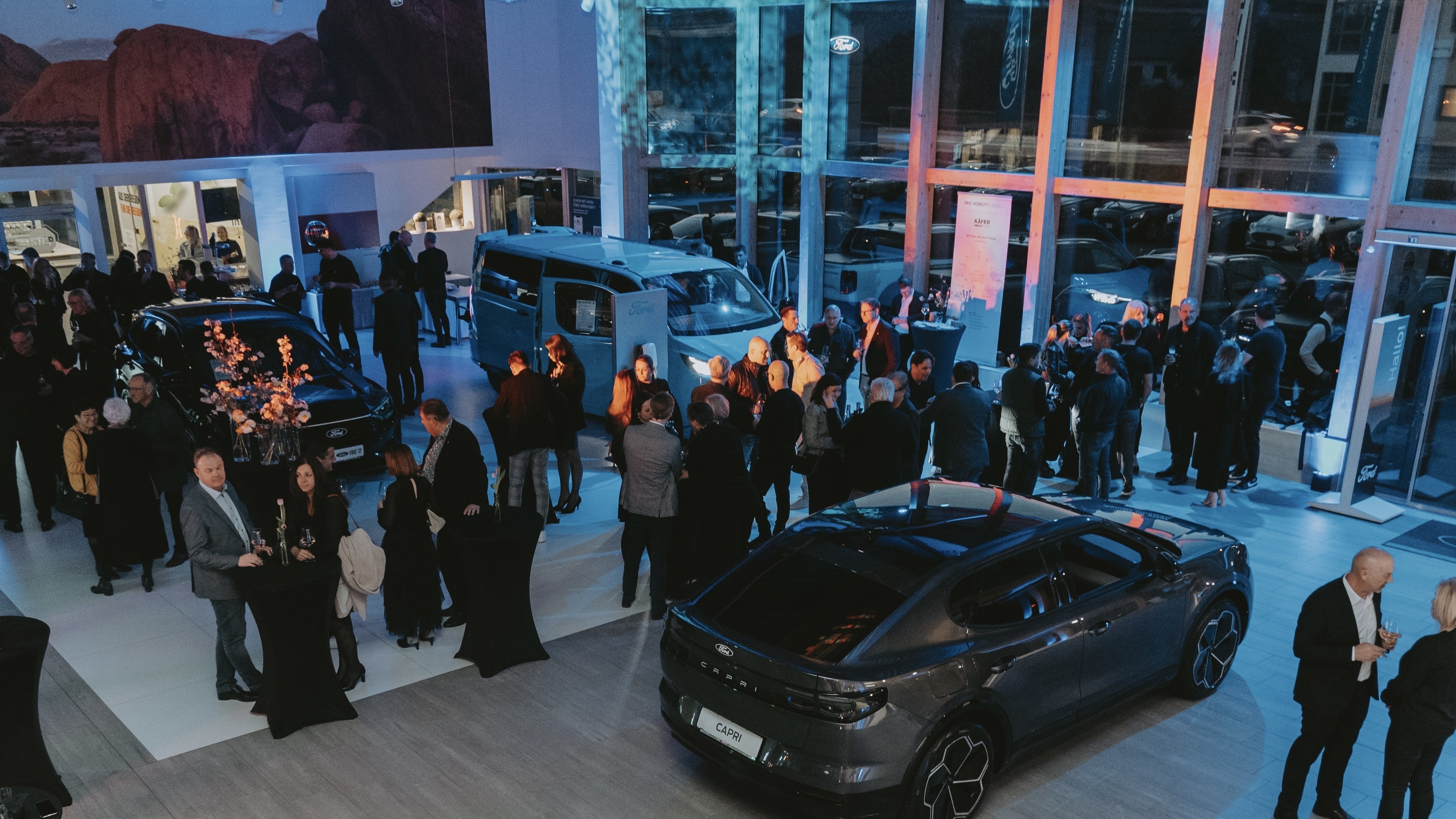Eine belebte Autoausstellung mit zahlreichen Gästen, modernen Autos und festlicher Beleuchtung in einem Showroom.