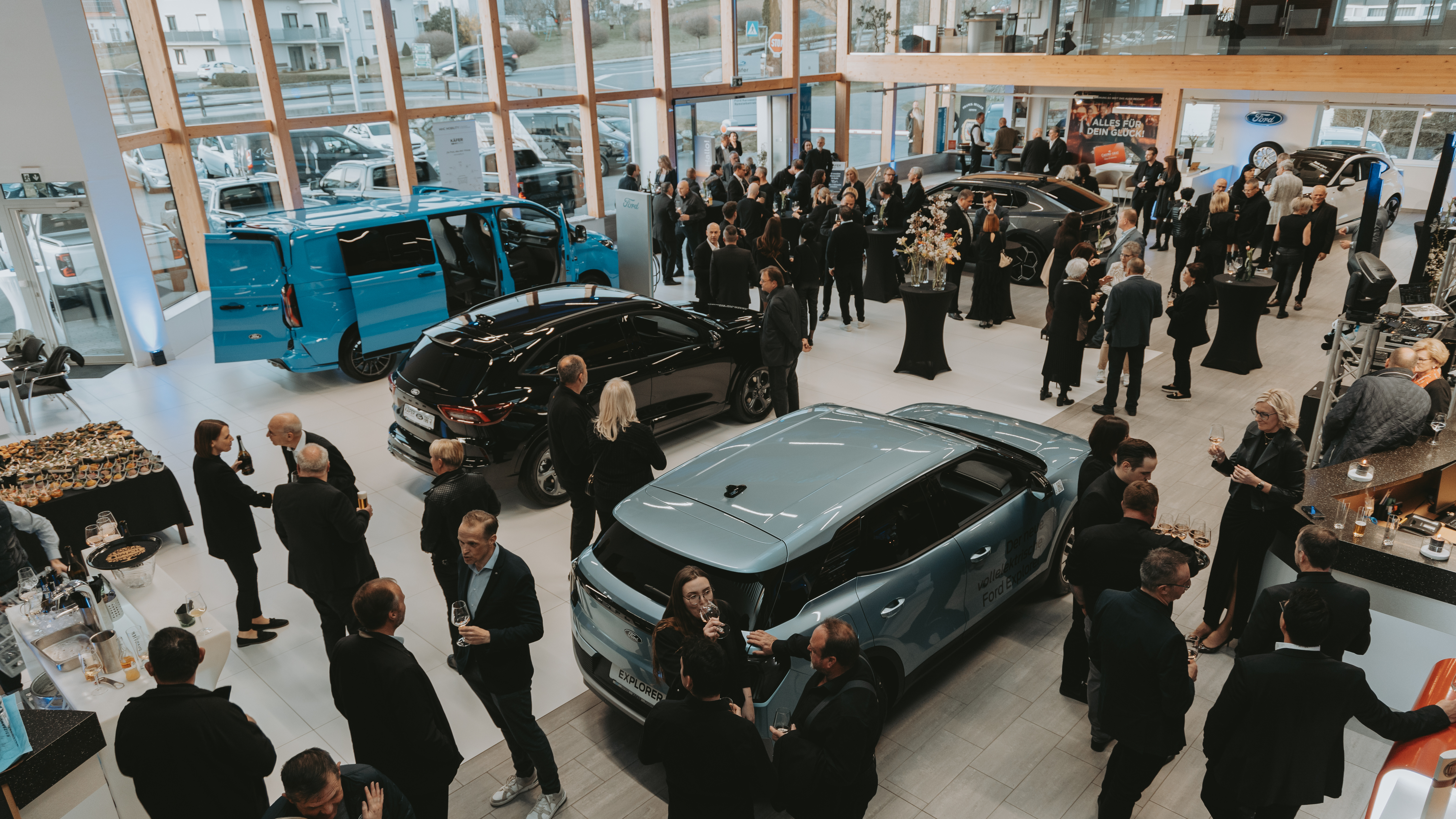 Voll besetzte Autohaus-Veranstaltung mit Gästen, eleganten Fahrzeugen und einem Buffet im Hintergrund.