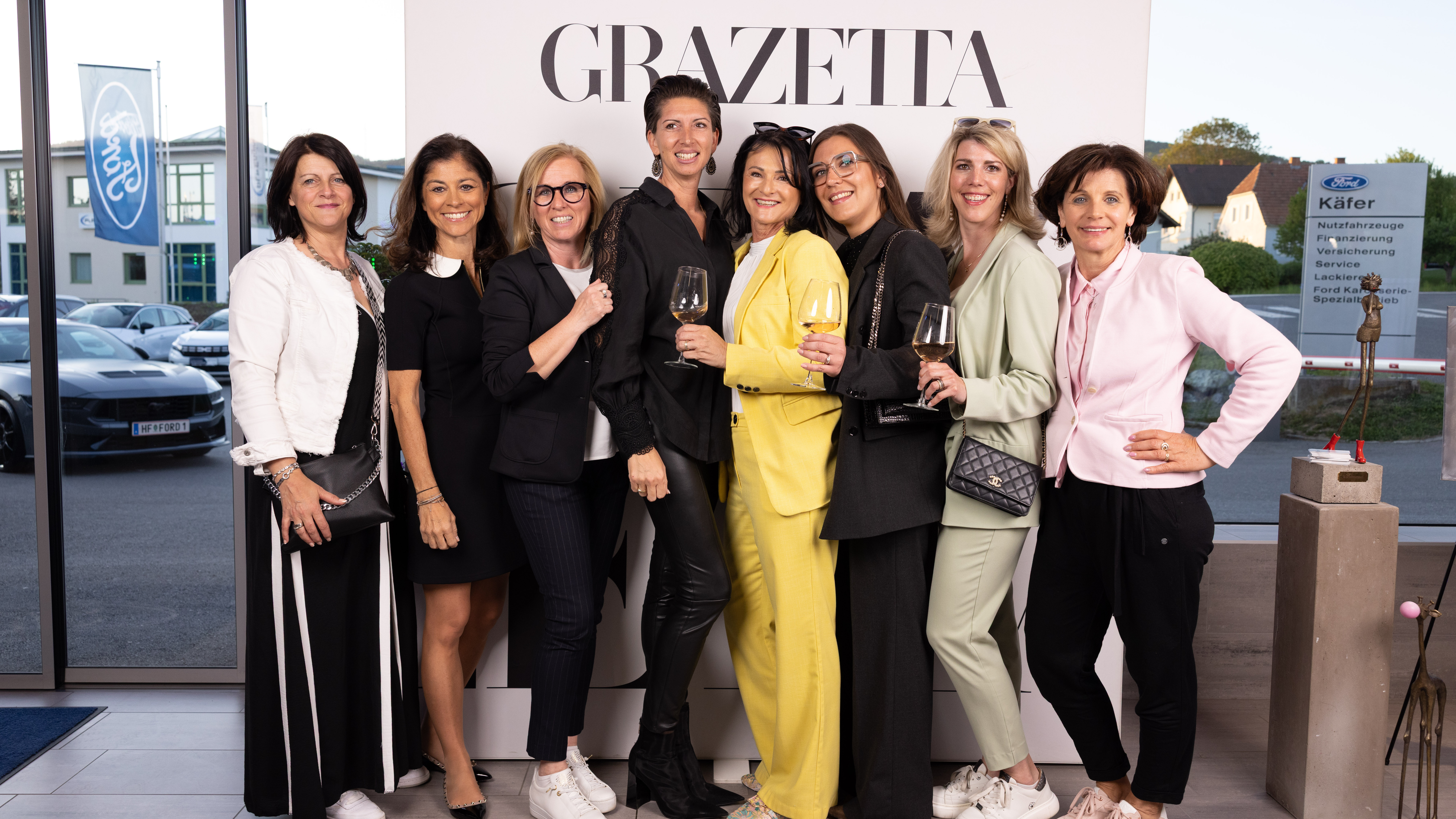 Eine Gruppe von Frauen posiert fröhlich vor einem GRAZETTA-Schild bei einer Veranstaltung.
