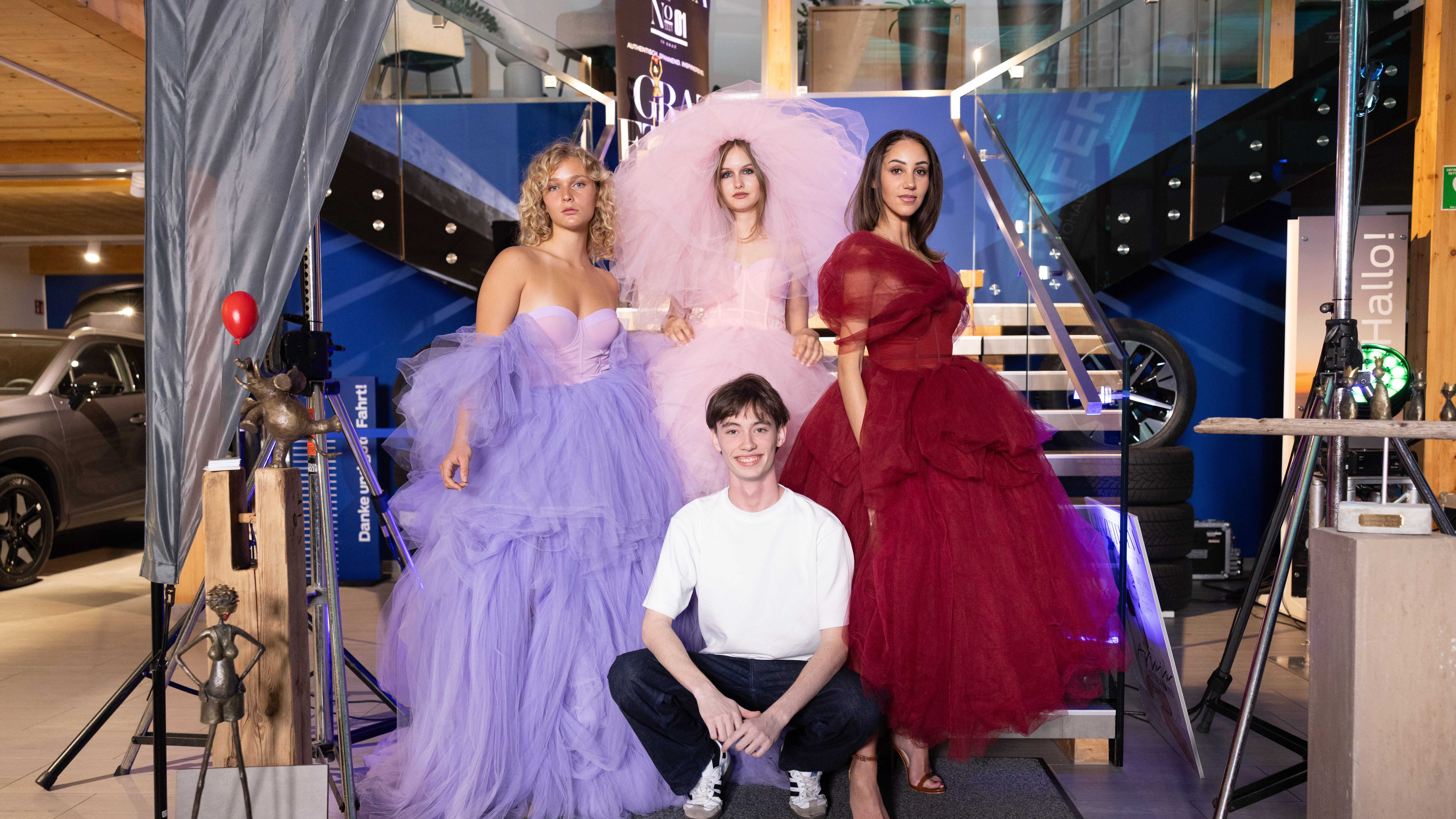 Modenschau mit vier Models in farbenfrohen Tüllkleidern, stehen vor einer Treppe in einem modernen Raum.