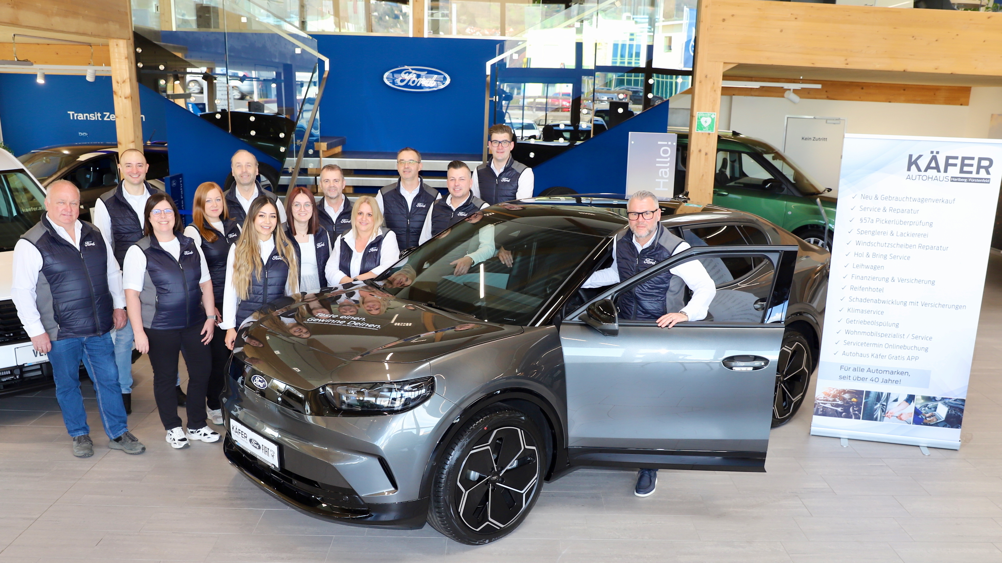 Gruppenfoto von Mitarbeitern bei Käfer Autohaus vor einem grauen Ford SUV in einem Autohaus.