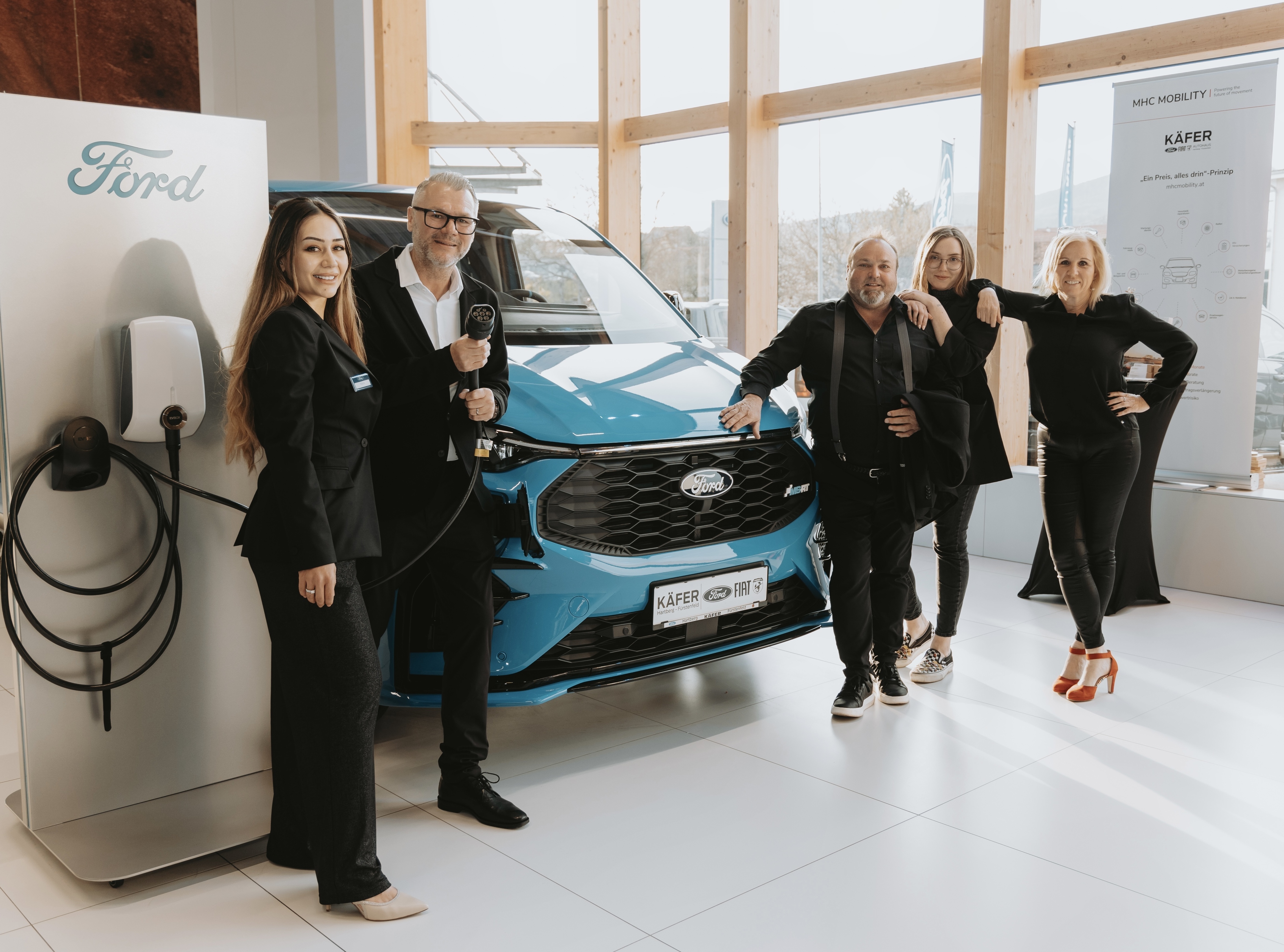 Ford-Mitarbeiter und eine blue Elektrofahrzeug beim Event präsentieren. Moderne Architektur im Hintergrund.